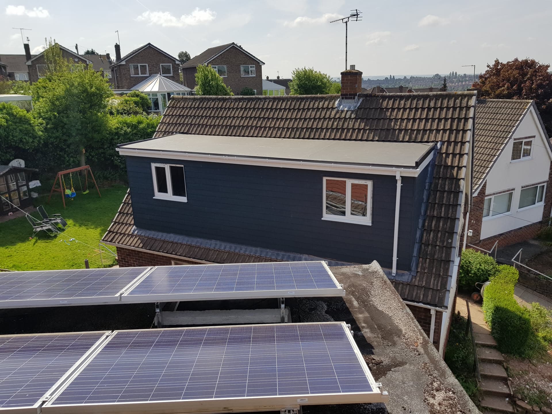 Flat roof extension with light grey covering on residential property with brown concrete tiled pitched roof
