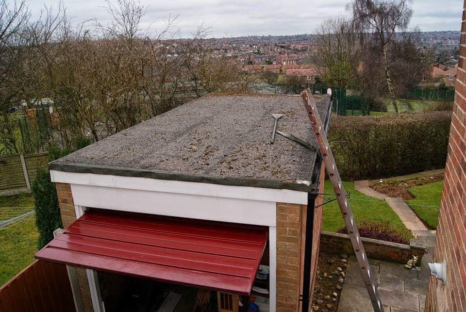 Flat roof with felt covering on garage with red metal canopy and ladder against side