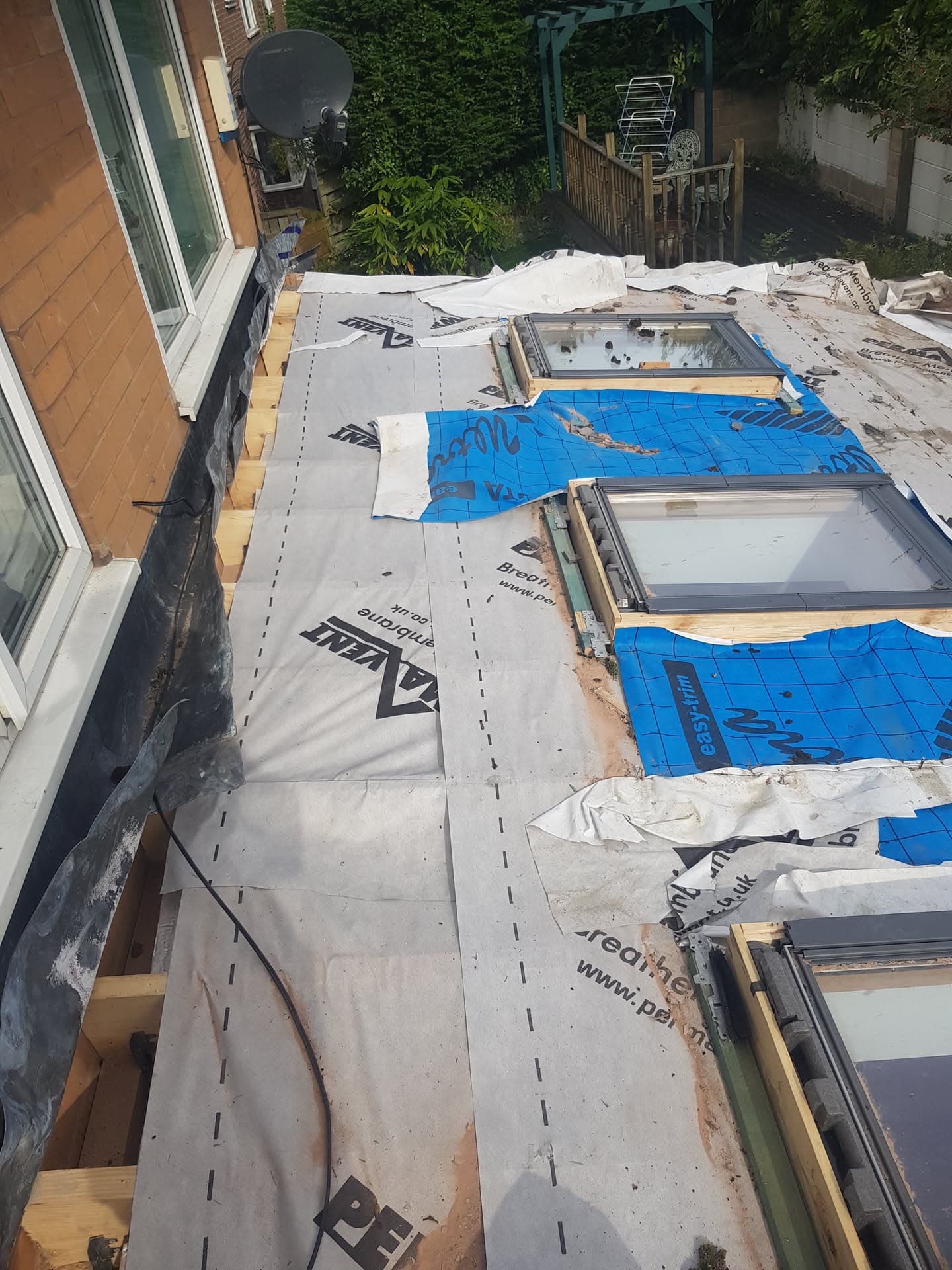 Flat roof installation in progress with breathable membrane and blue vapour barrier around three roof windows