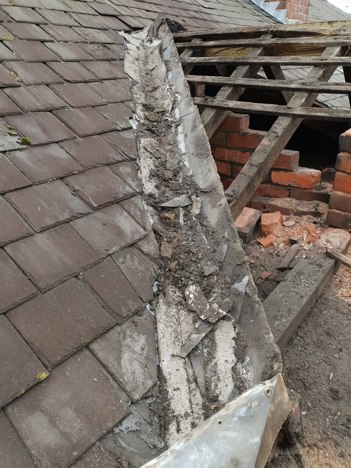 Damaged pitched roof with exposed timber battens and deteriorated concrete ridge tiles requiring repair