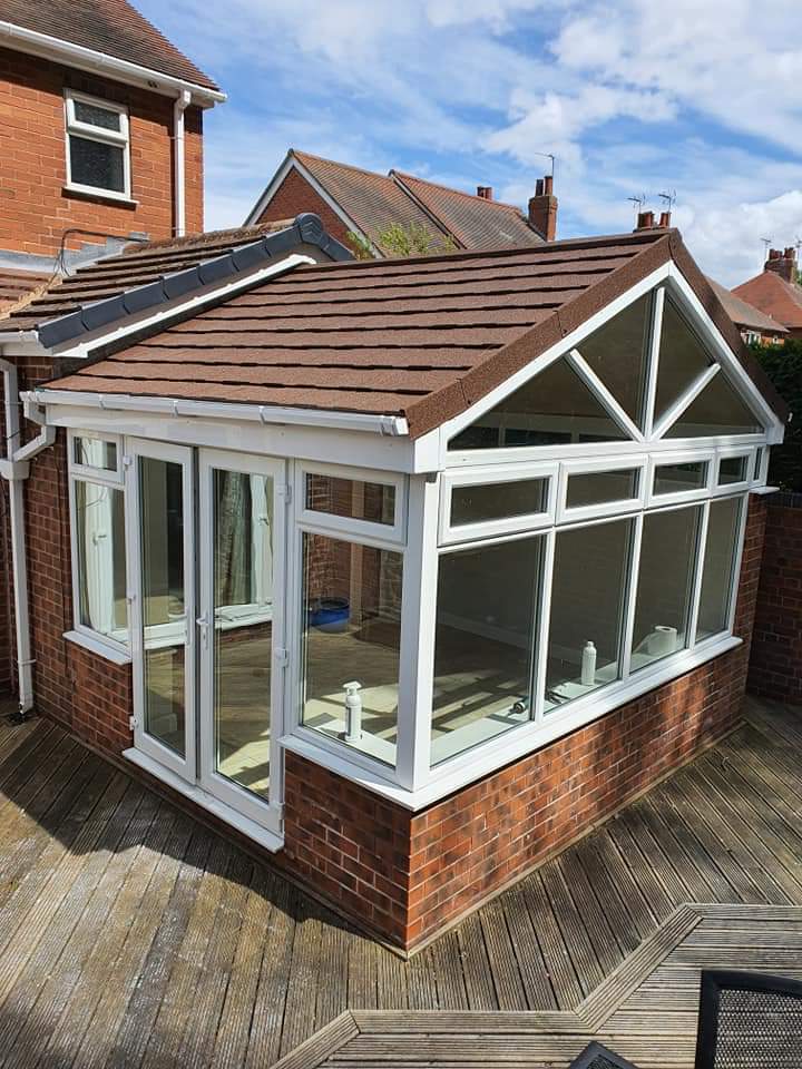 Conservatory with brown tiled roof, white uPVC frames and guttering on decking