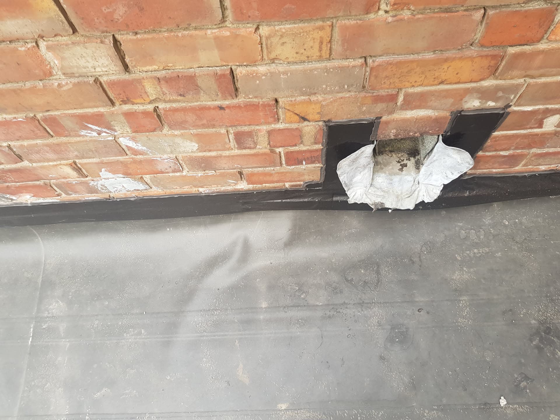 Damaged lead flashing at chimney base showing deterioration and temporary repair