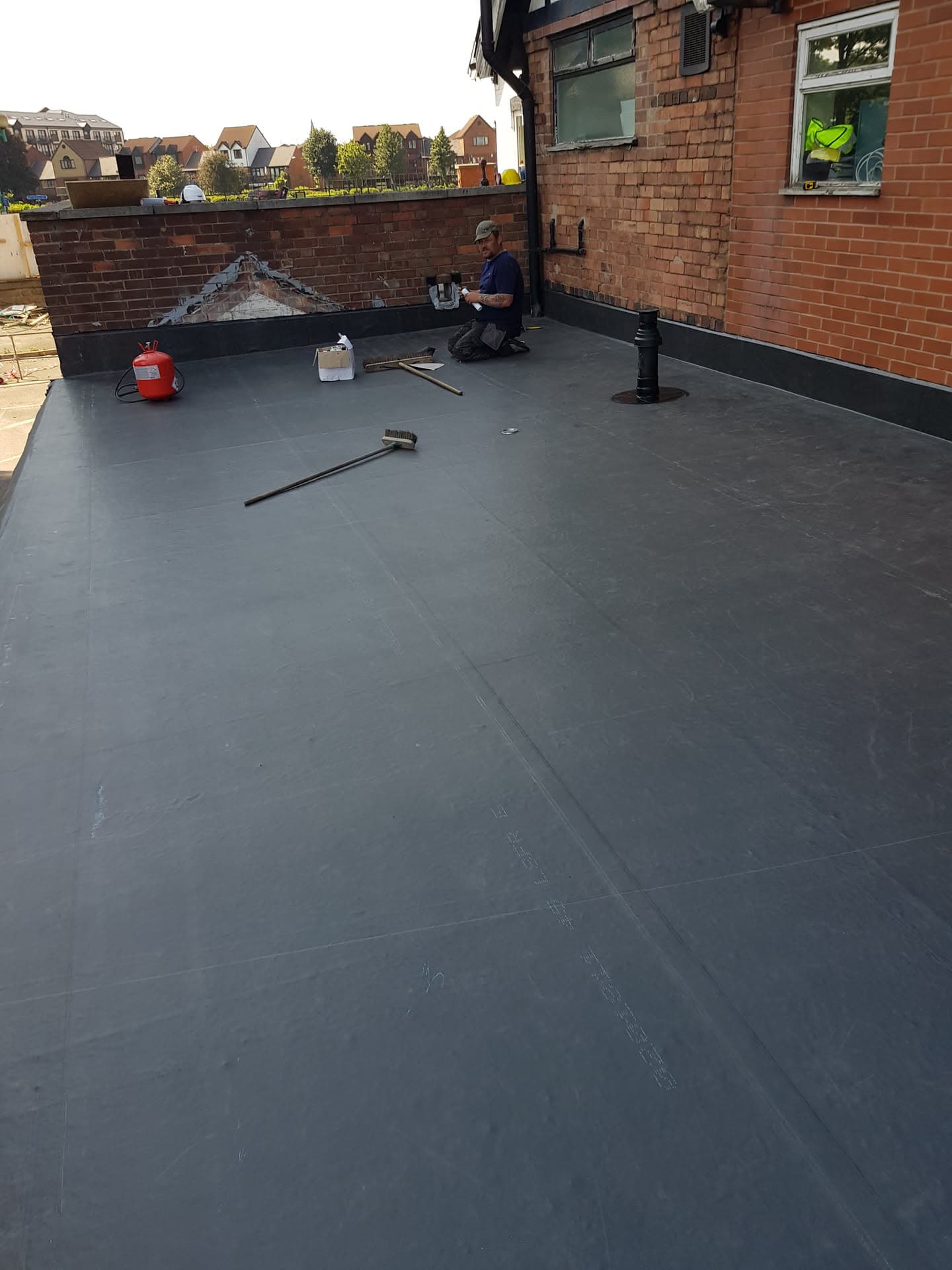 Fitter installing grey EPDM rubber membrane on flat roof extension