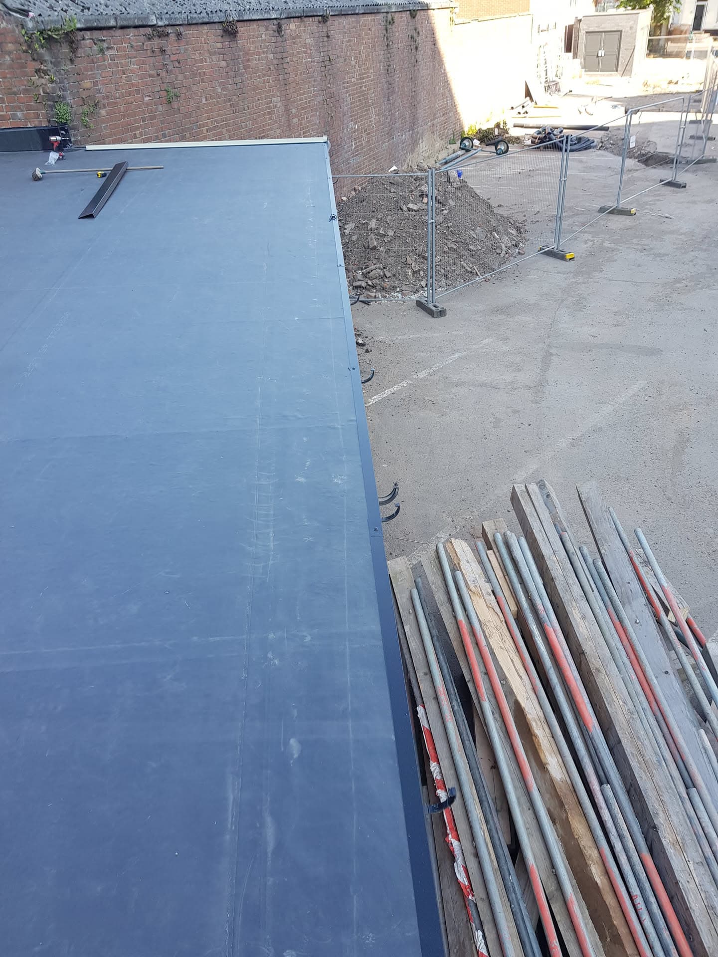 Grey GRP flat roof with scaffolding boards and temporary fencing on adjacent ground