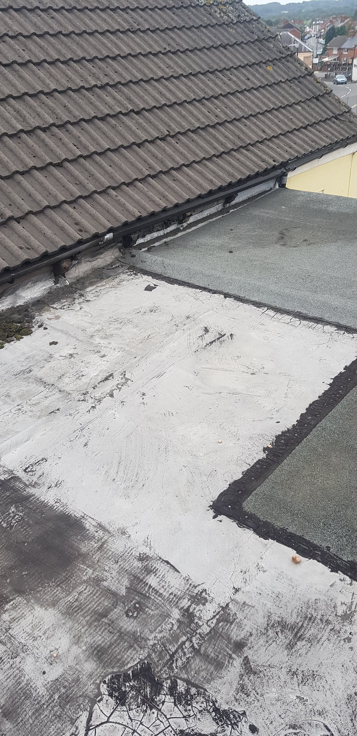 Pitched roof with brown concrete tiles and black guttering alongside flat roof section