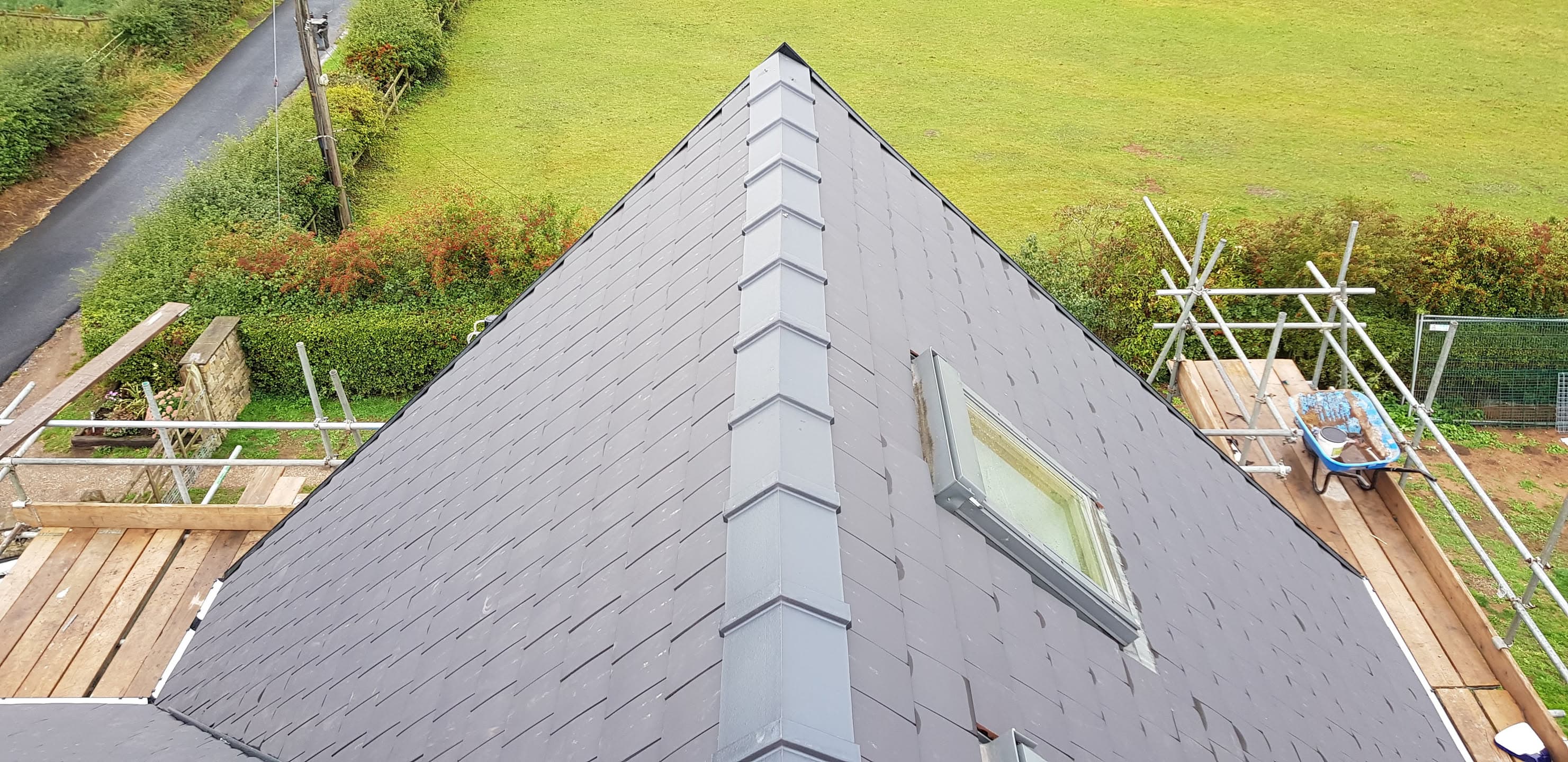 Pitched slate roof with ridge tiles and roof window, scaffolding visible