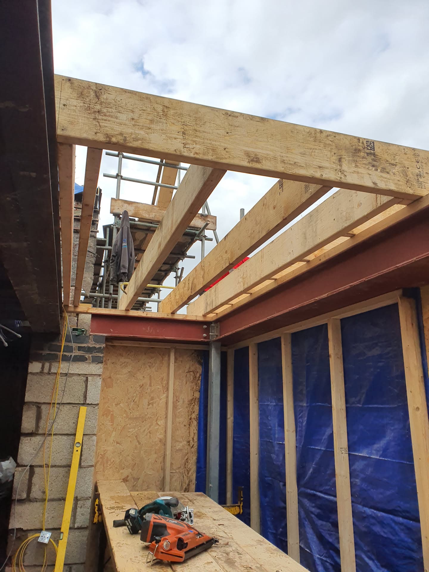 Timber frame construction with exposed roof joists and red steel beam during flat roof installation