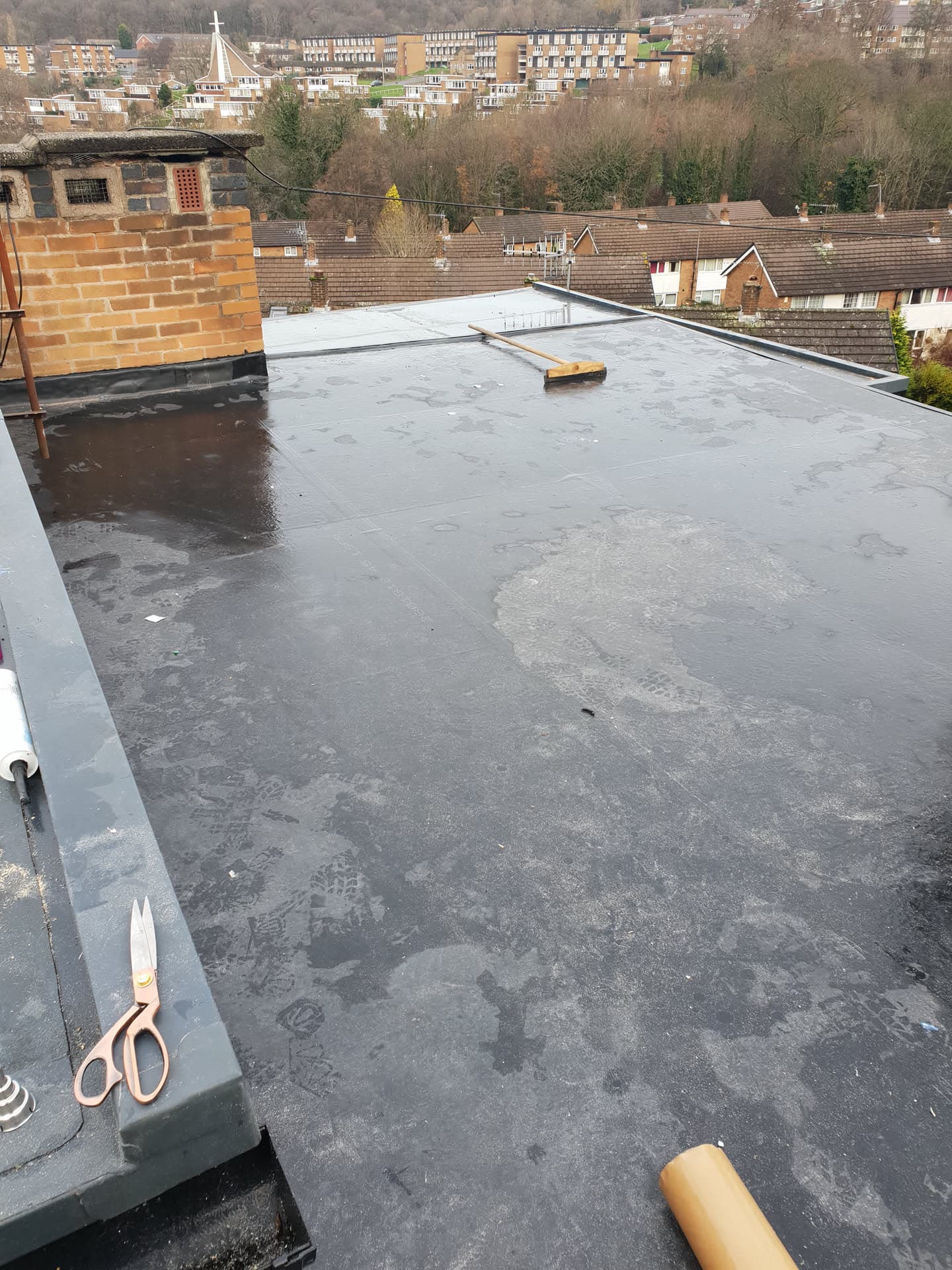 Grey flat roof with felt membrane and chimney stack overlooking residential area