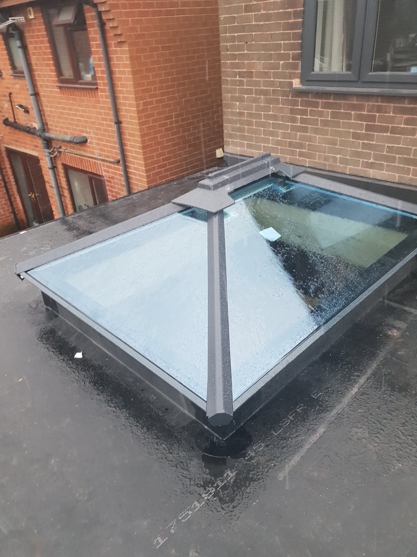 Flat roof with grey GRP fibreglass finish and glass rooflight panel between brick buildings