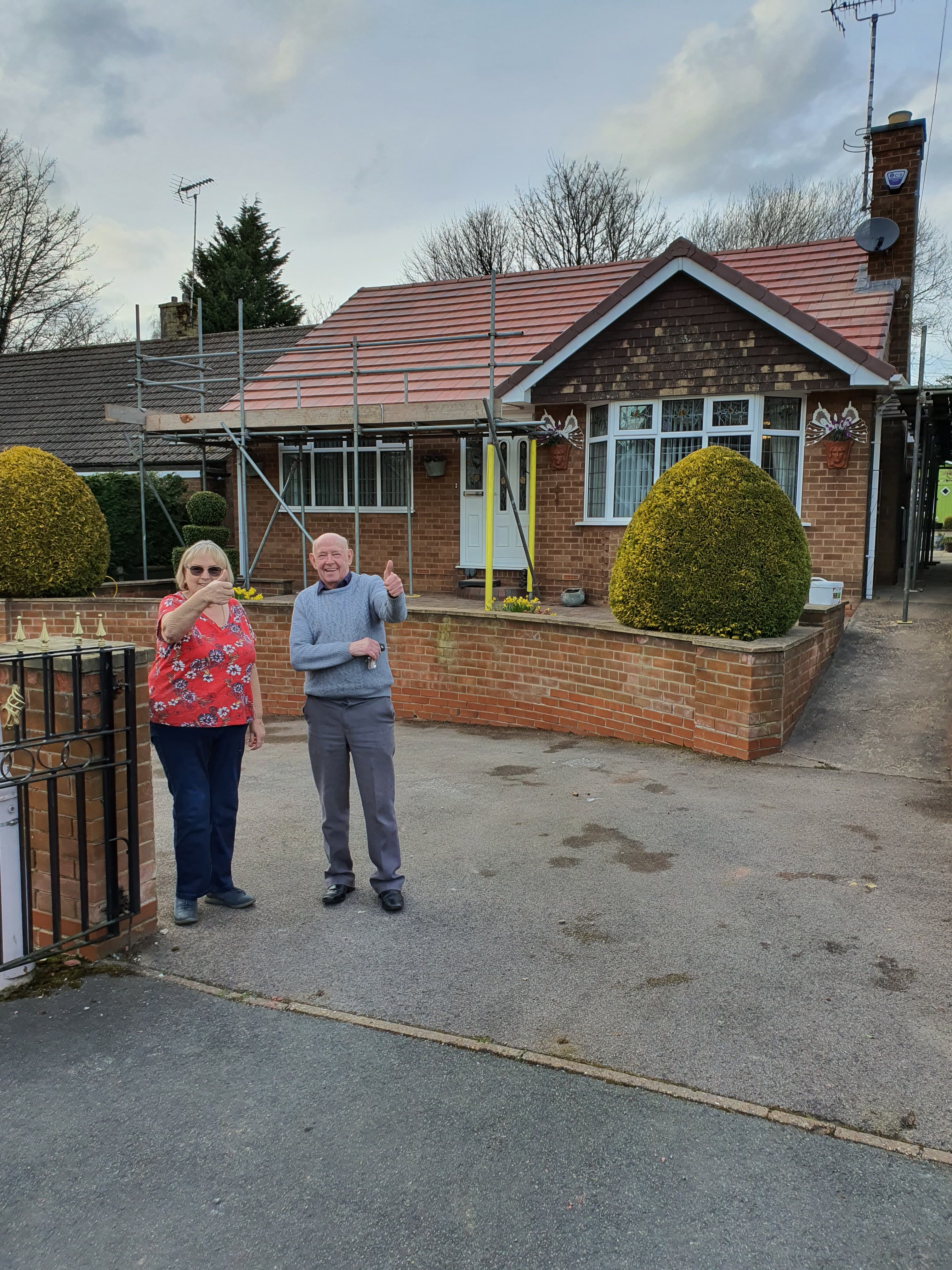 Completed pitched roof with red concrete tiles and scaffolding on brick bungalow with chimney