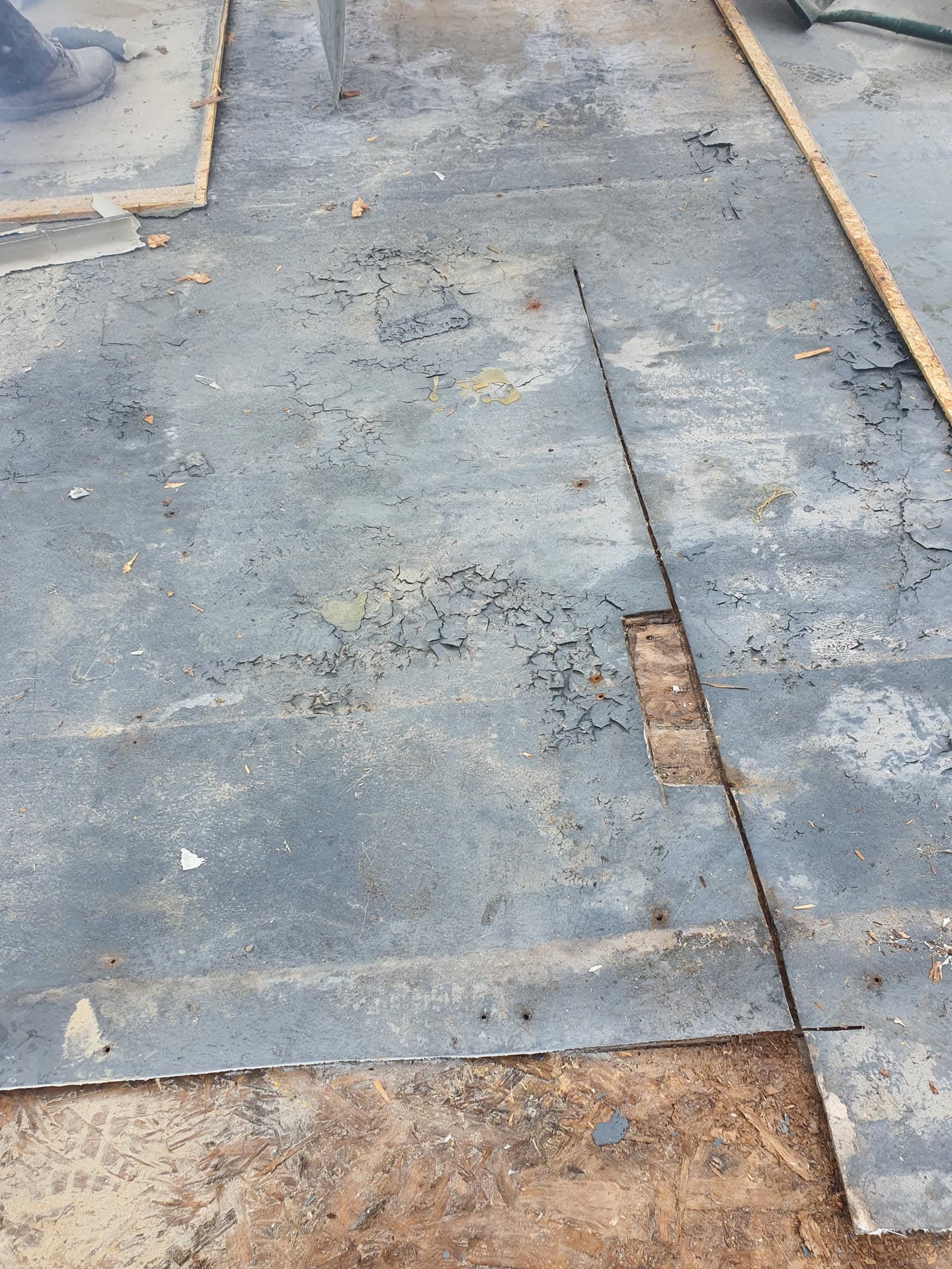 Worn grey felt flat roof showing cracking and deterioration requiring replacement