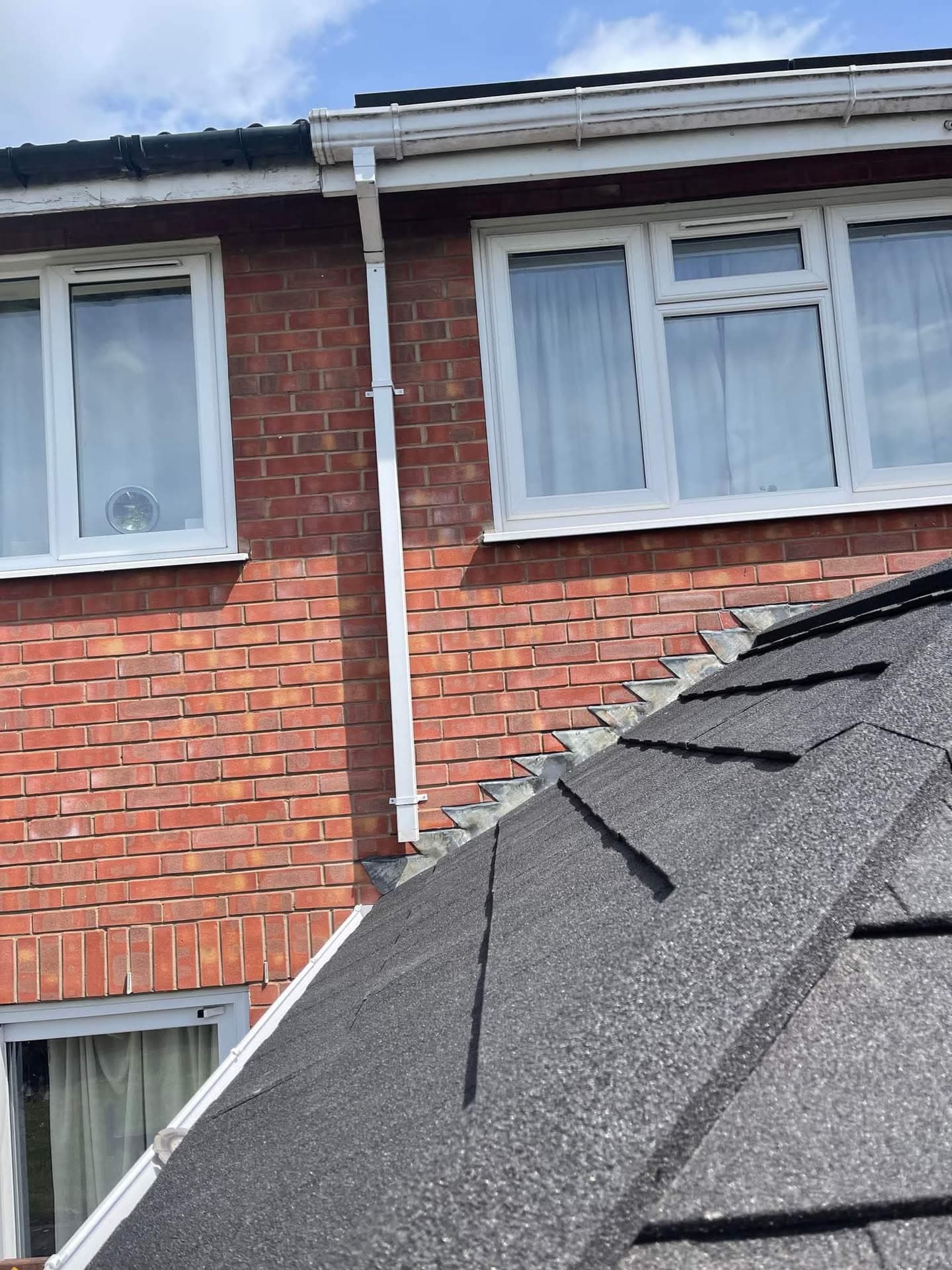 Pitched roof with grey felt tiles, white fascias, soffits and guttering on red brick house