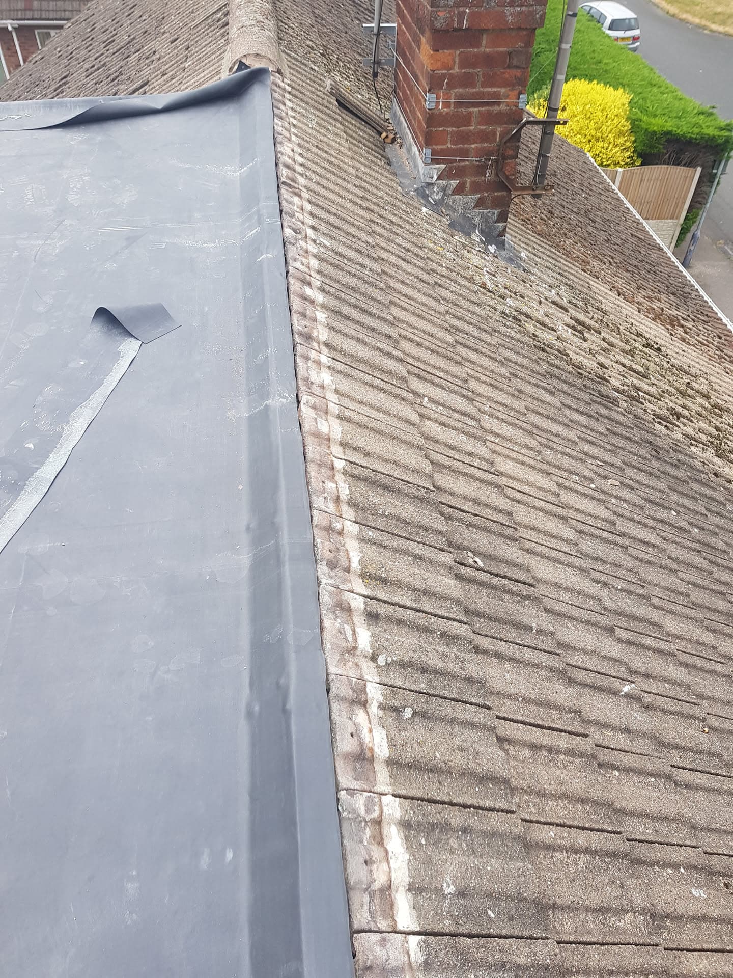 Grey flat roof with lead flashing meeting weathered concrete tiled pitched roof and brick chimney