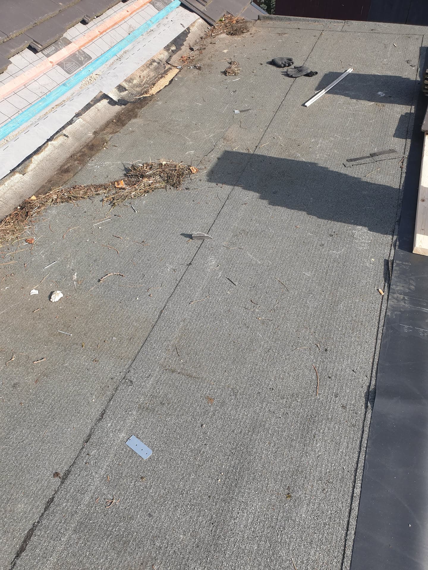Flat roof with grey felt covering showing debris and patches requiring repair
