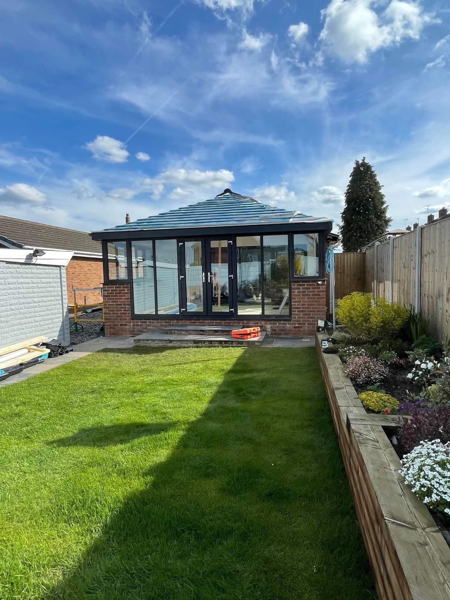 Modern conservatory extension with blue metal standing seam roof and black framed glass walls