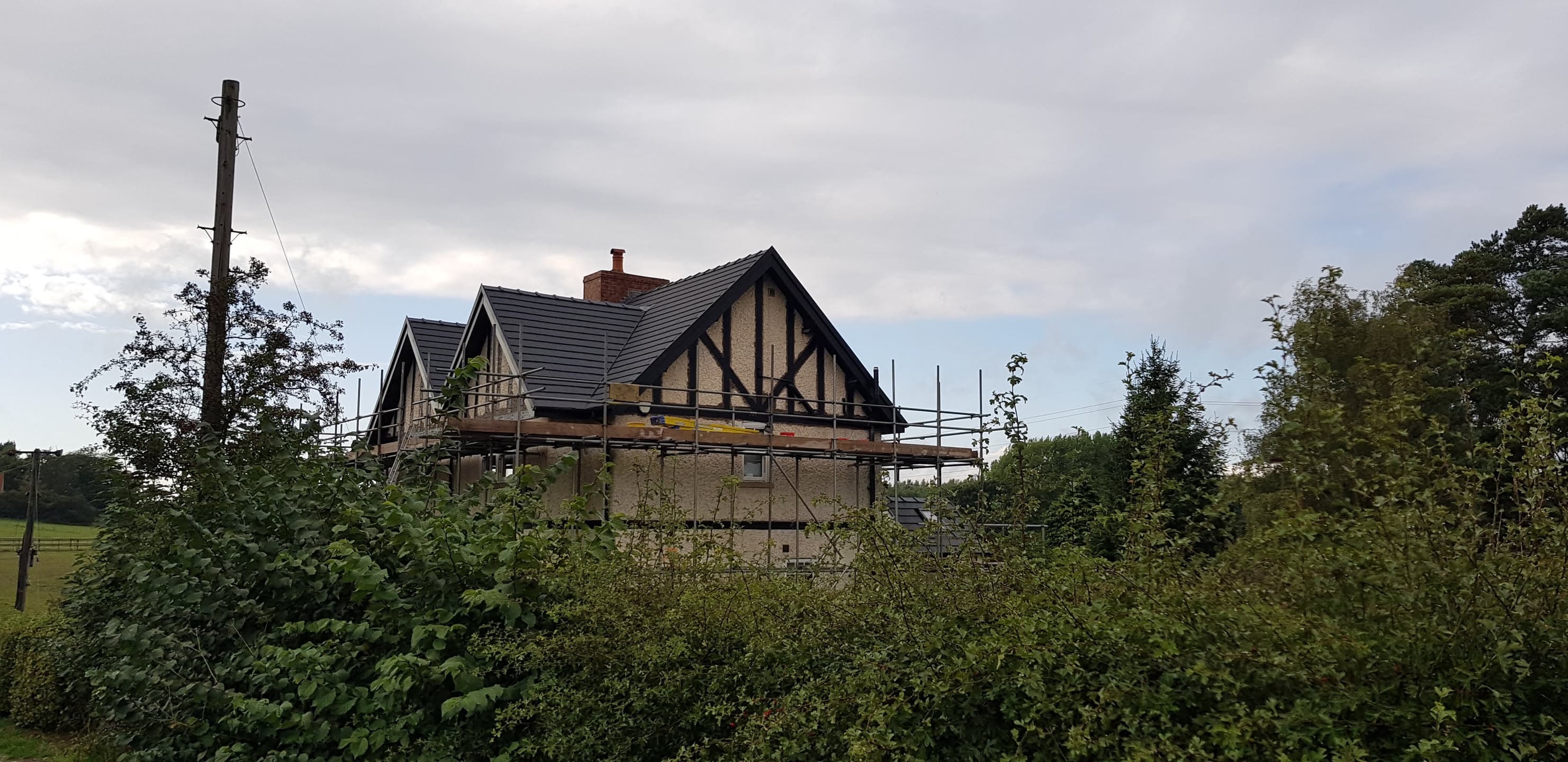 Tudor-style house with dark tiled pitched roof and chimney stack, scaffolding erected around property
