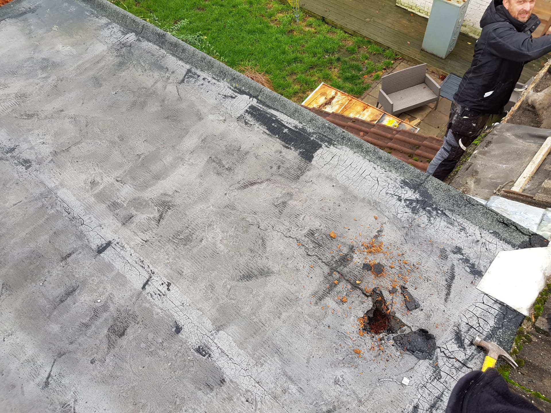 Flat roof repair in progress with felt membrane and fitter working on edge