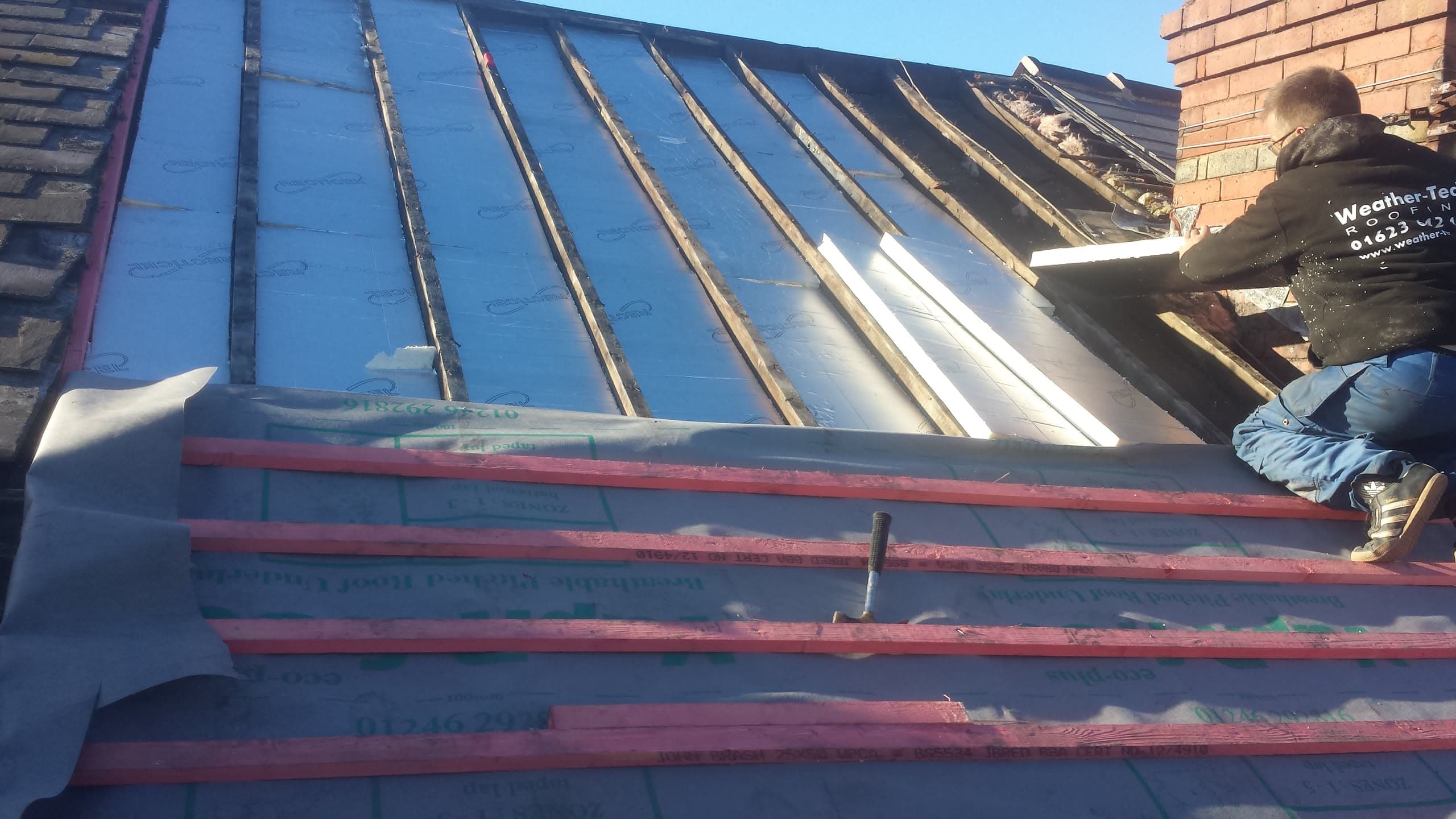 WeatherTech fitter installing battens on pitched roof with blue membrane and chimney stack