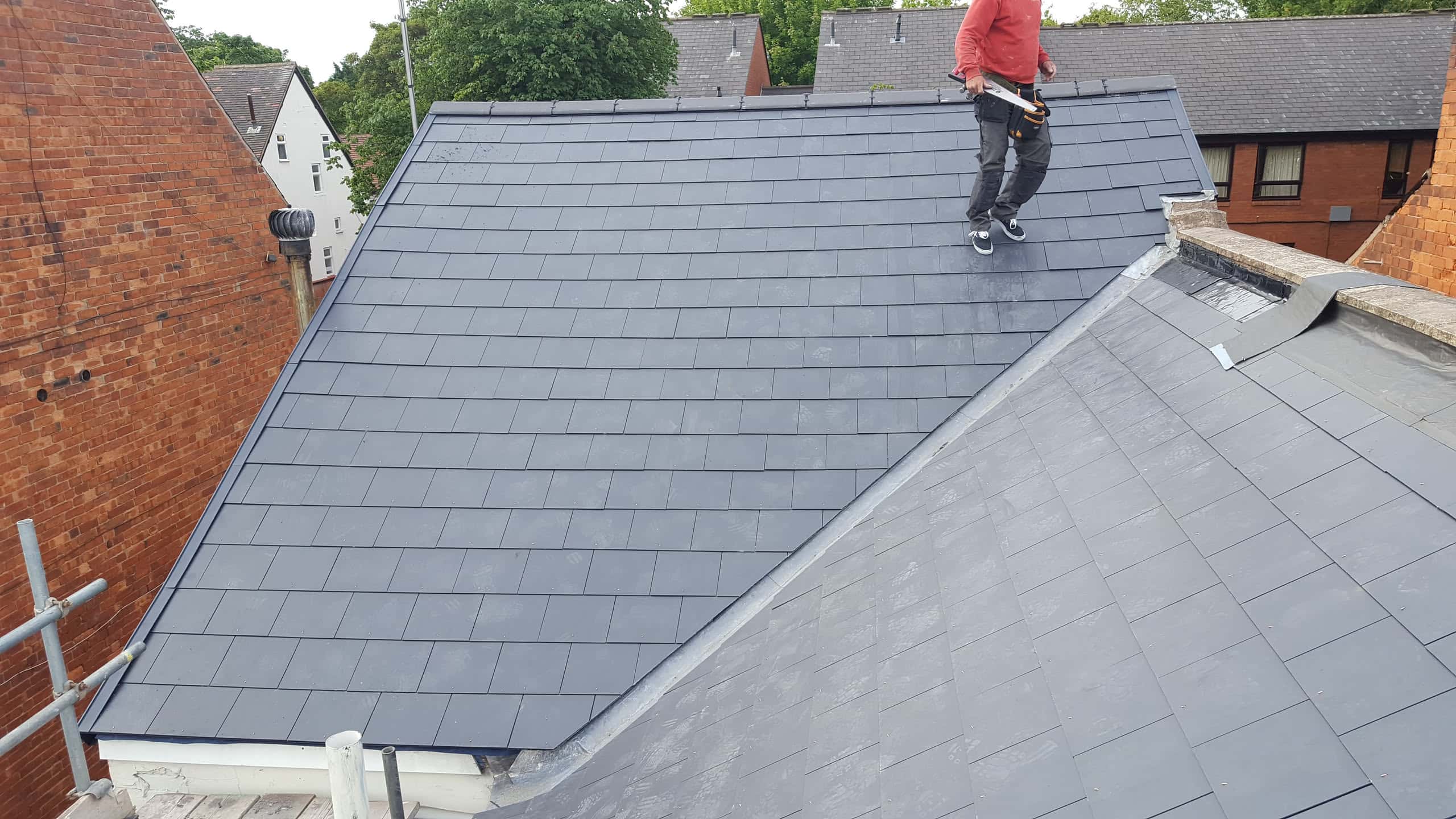 Fitter standing on newly completed grey slate pitched roof with ridge detail