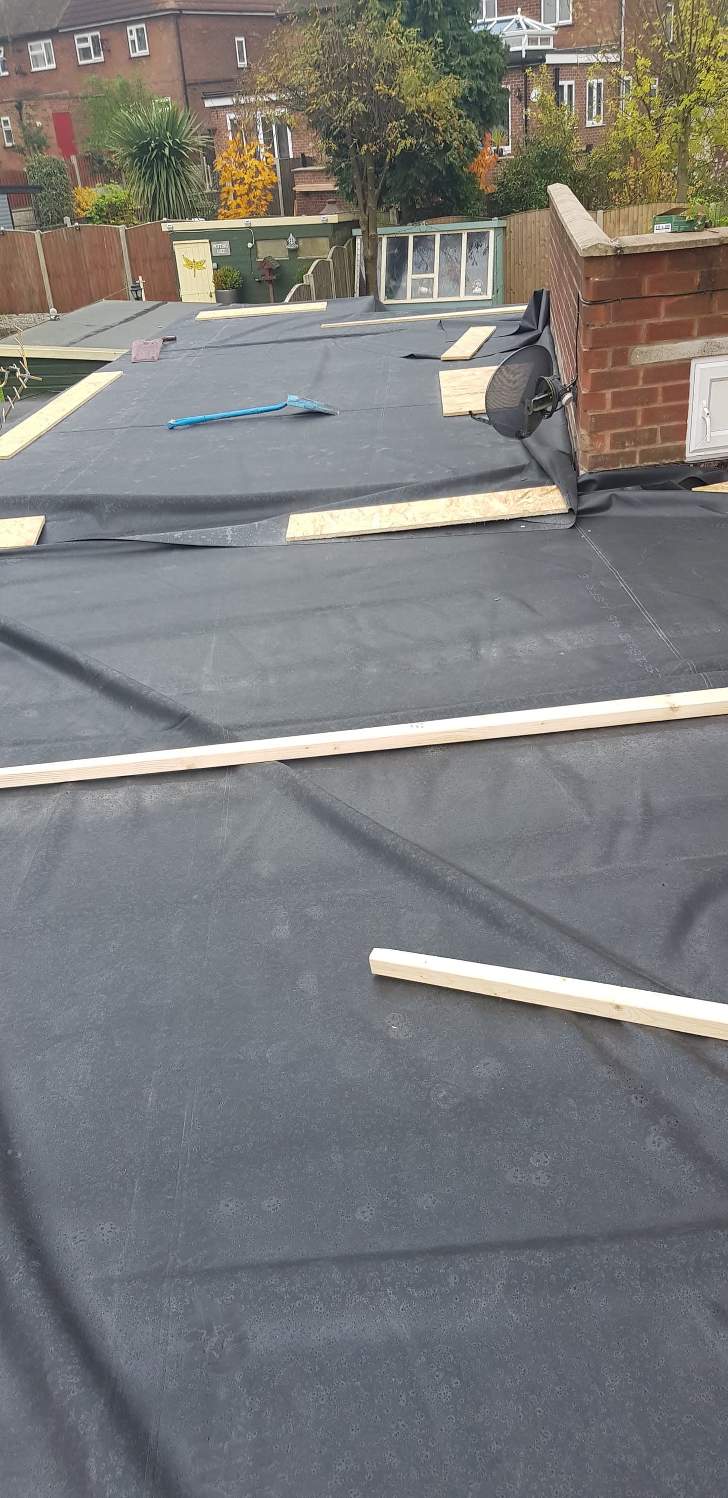 Flat roof installation in progress with dark grey felt membrane and timber edging