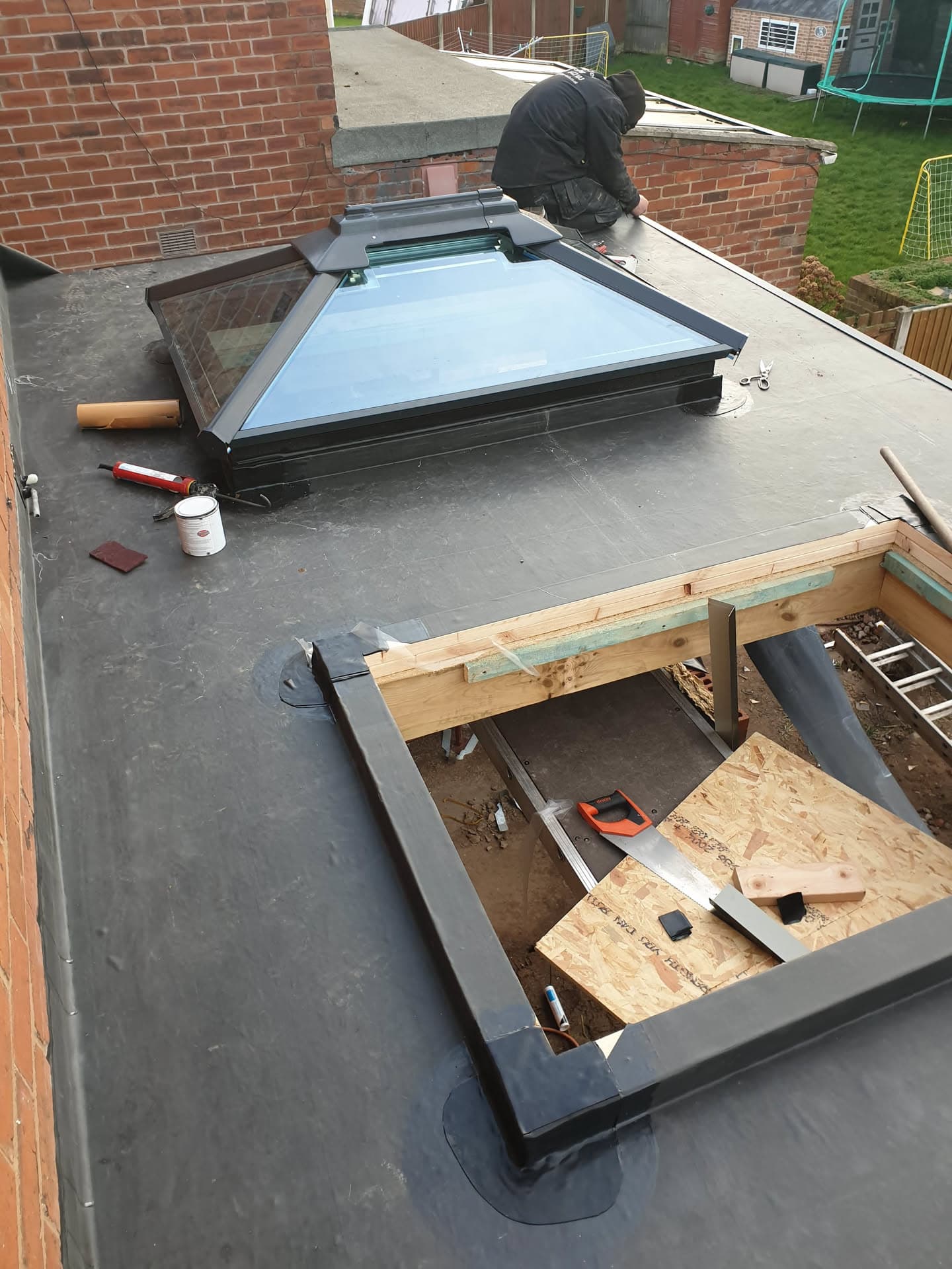 Fitter installing skylight on flat roof with grey felt covering and timber frame