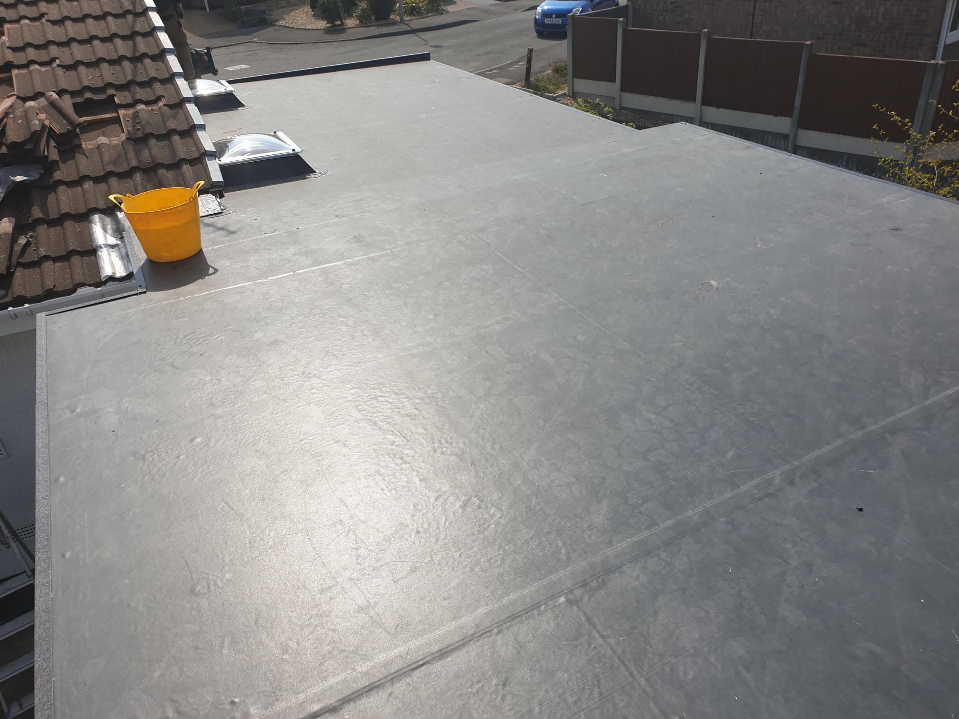 Grey flat roof with GRP fibreglass finish and roof light, adjacent to brown tiled pitched roof