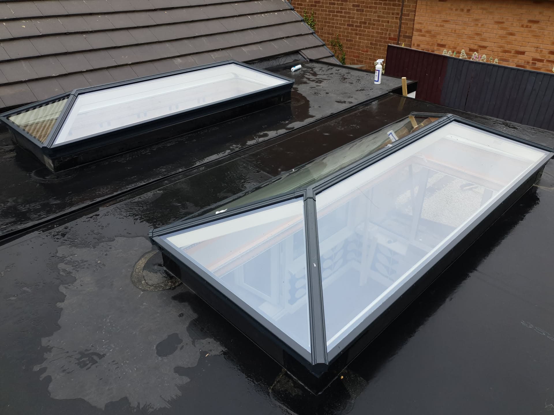 Flat roof with three aluminium-framed roof lights installed on dark felt surface