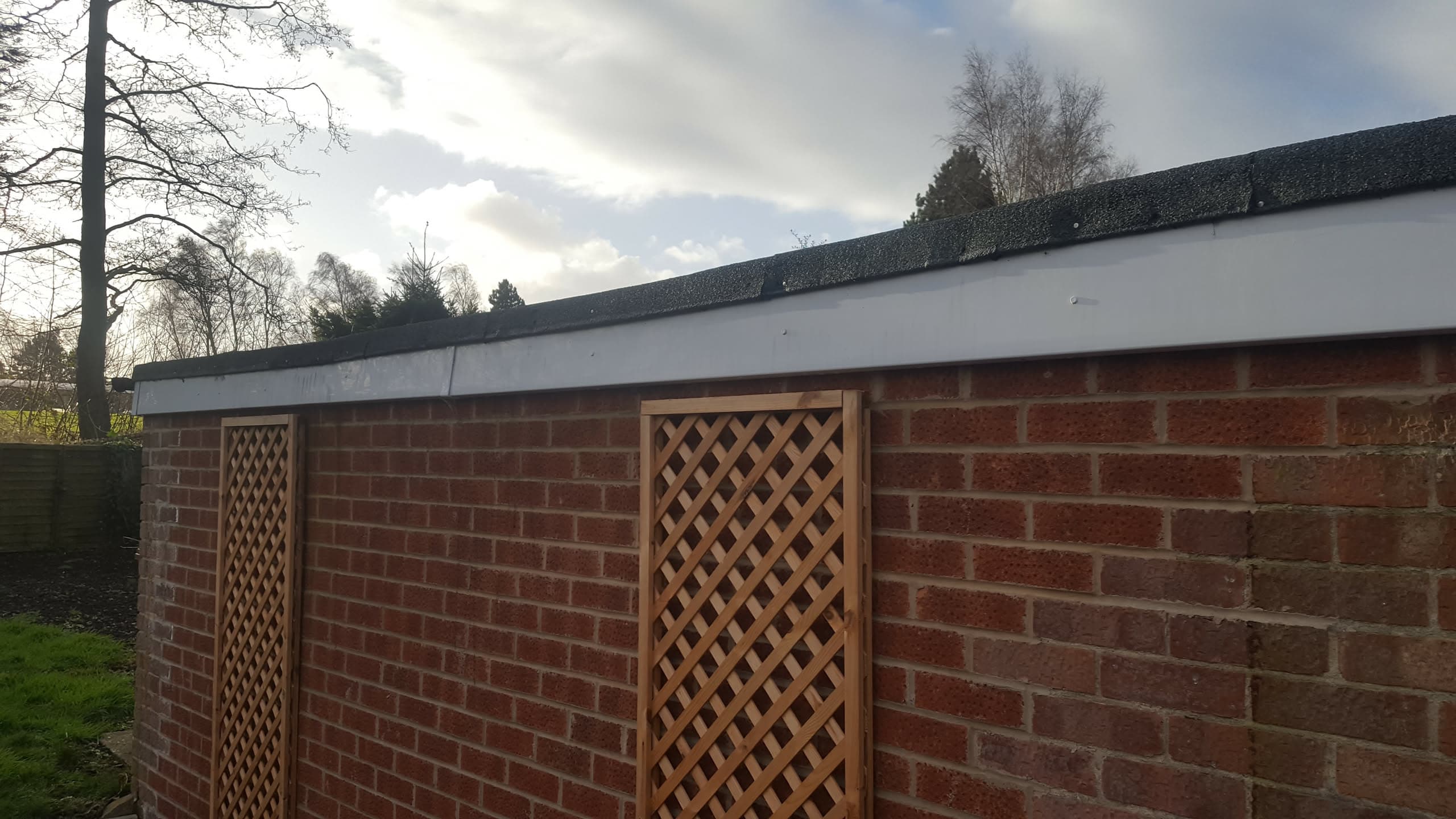 Flat roof with white fascia board on brick outbuilding