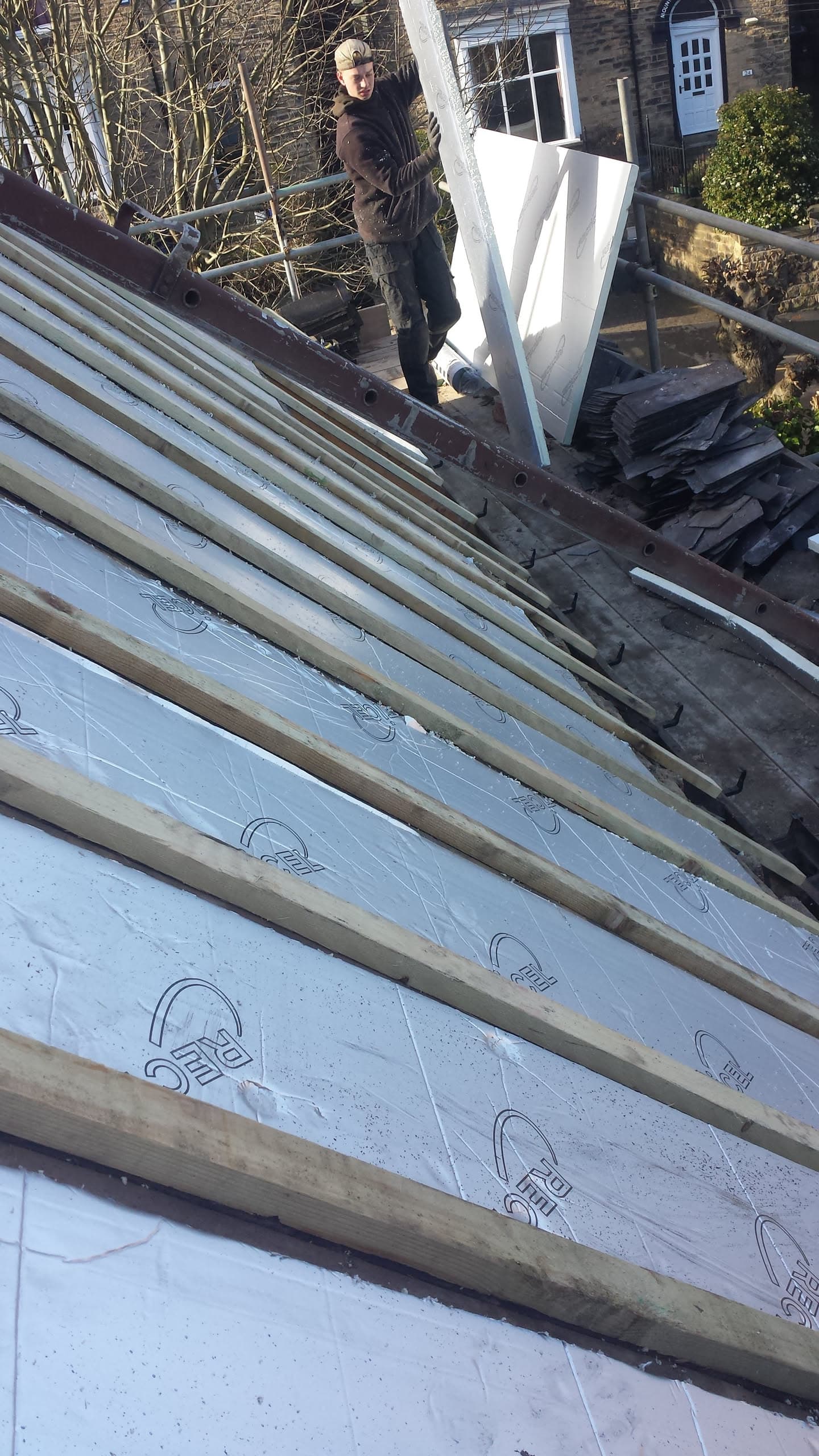 Fitter working on pitched roof with exposed battens and breathable membrane during re-roofing