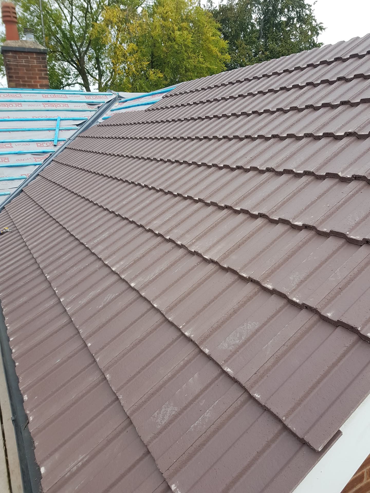 Pitched roof with brown concrete tiles and blue roofing membrane visible at ridge