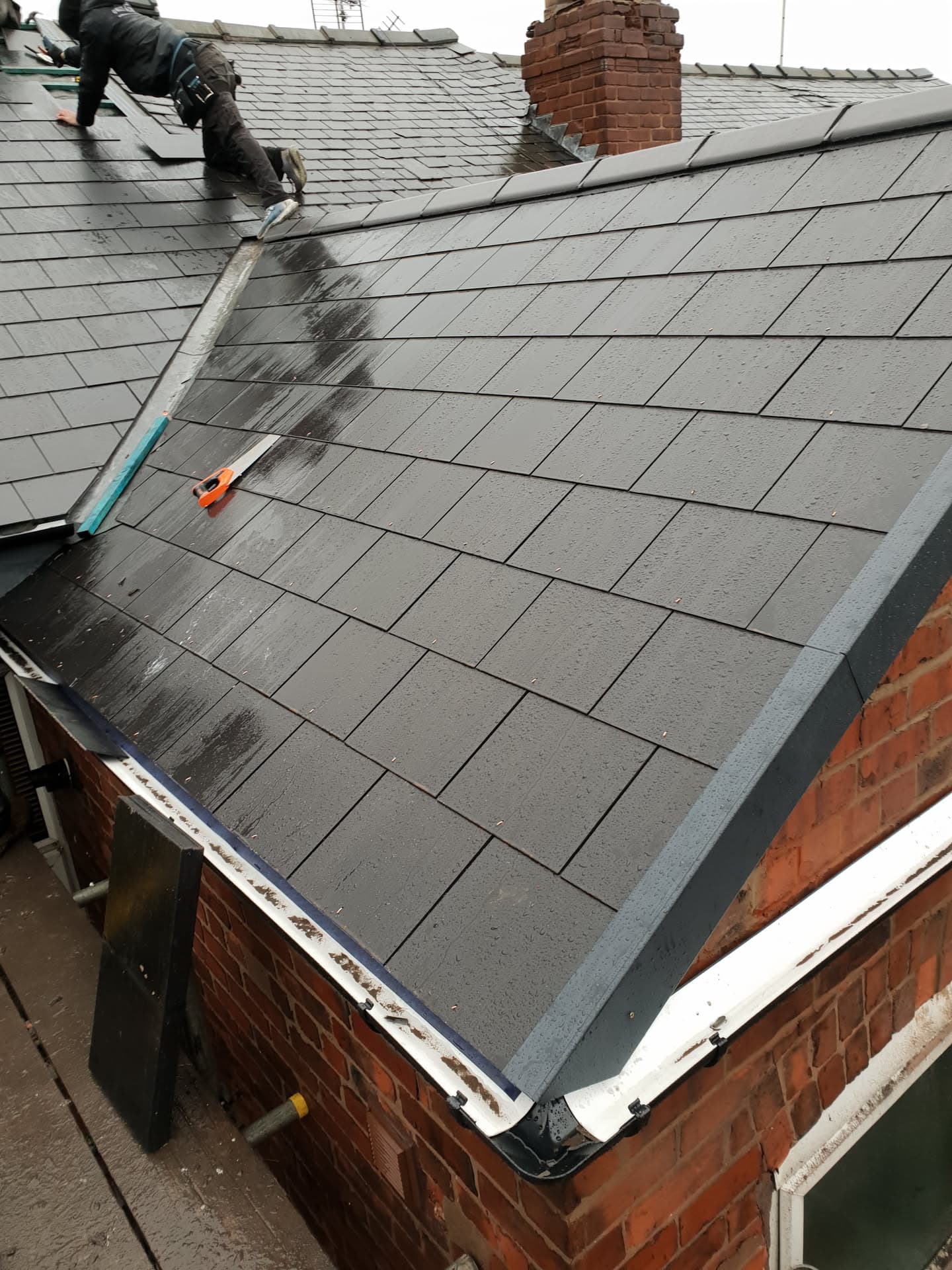 Fitter installing grey slate tiles on pitched roof with brick chimney stack