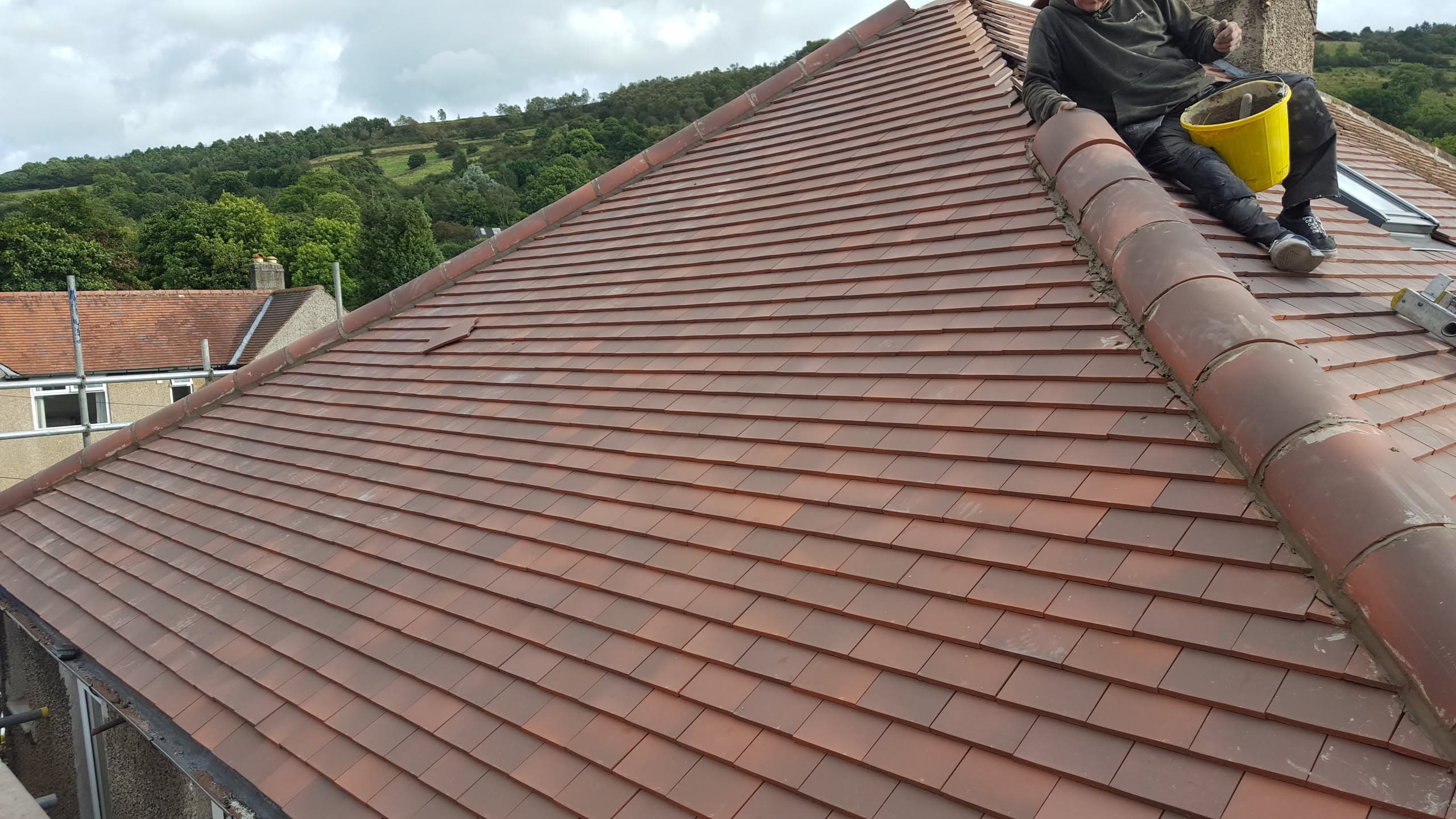 Fitter working on pitched roof with terracotta clay tiles and ridge tiles