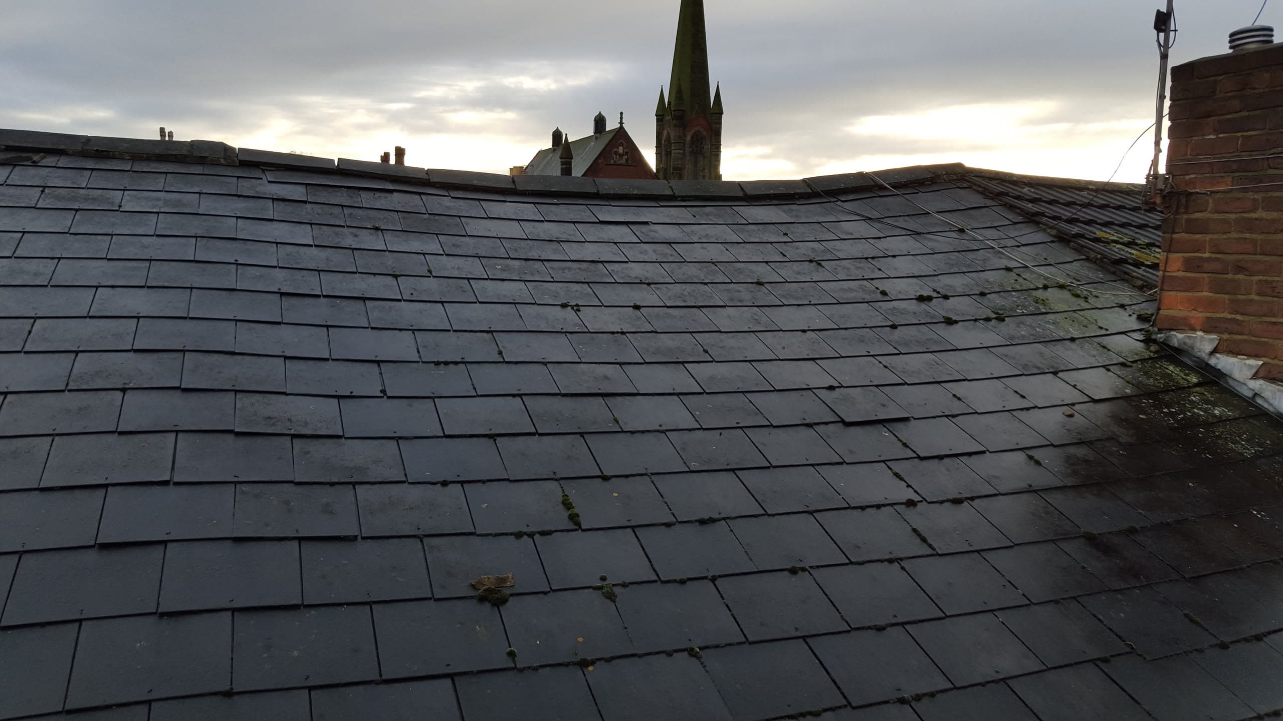 Pitched roof with dark grey slate tiles and brick chimney stack