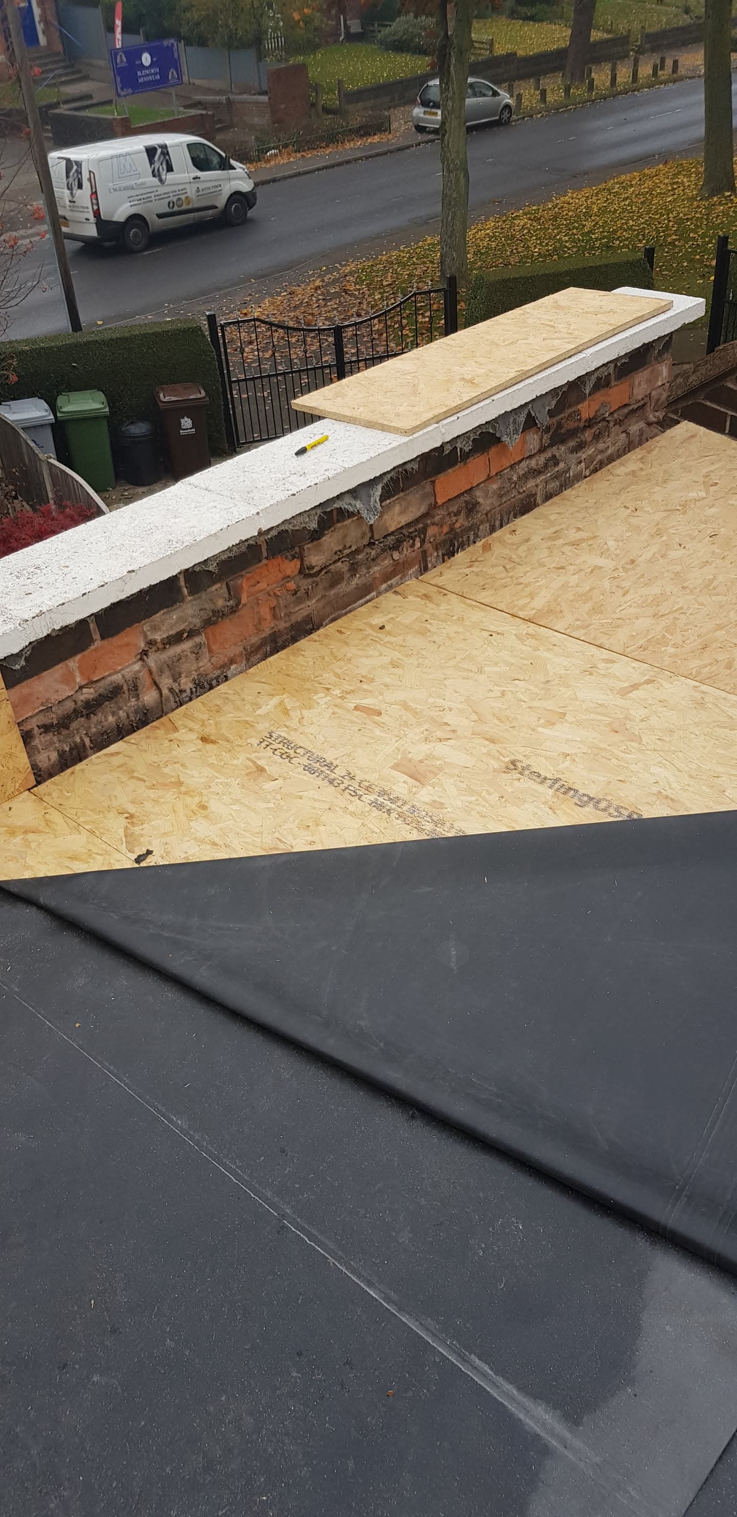 Flat roof installation with EPDM rubber membrane and OSB decking around brick parapet wall