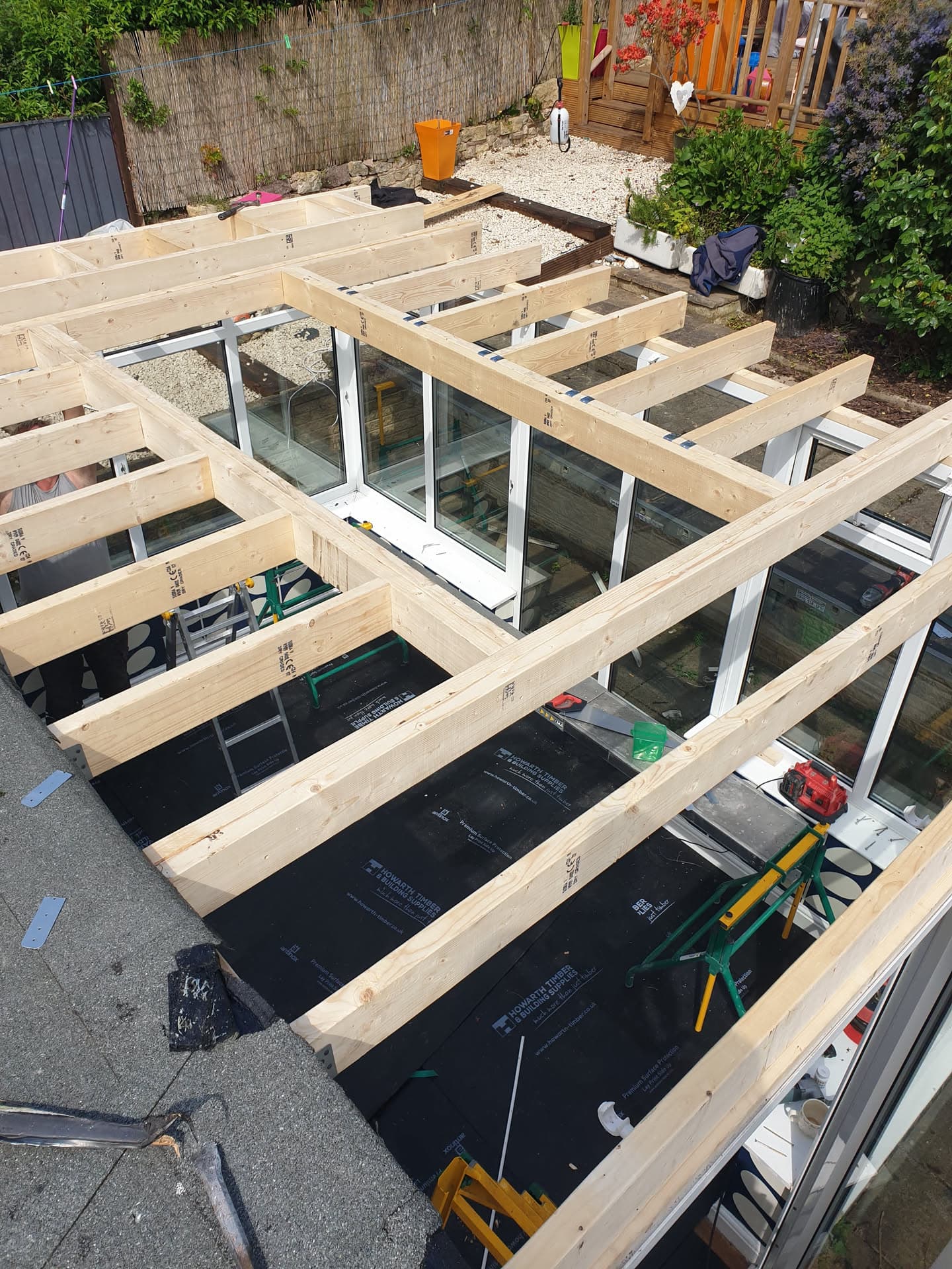 Flat roof construction in progress with timber joists and black felt membrane over conservatory
