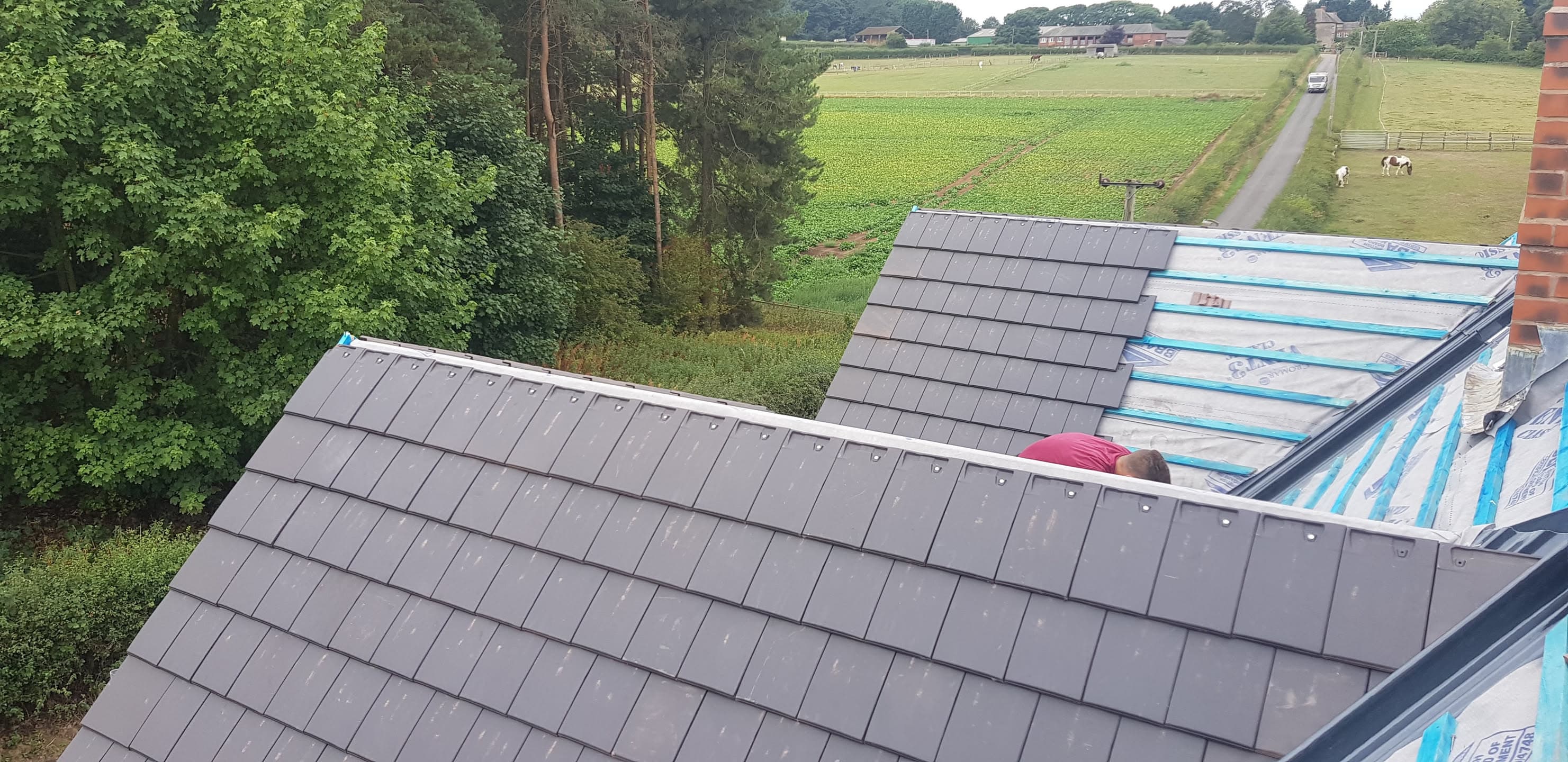 Pitched roof with grey slate tiles being installed, fitter working on blue membrane underlay