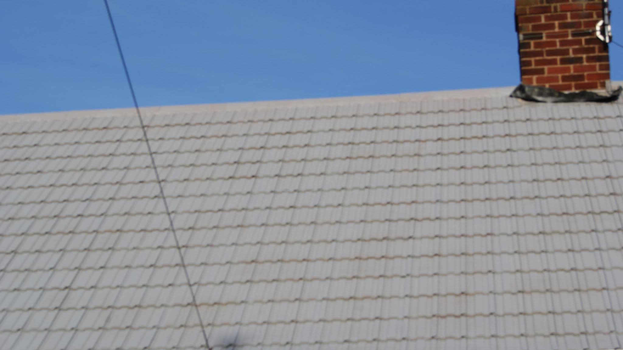 Pitched roof with light grey concrete tiles and brick chimney stack