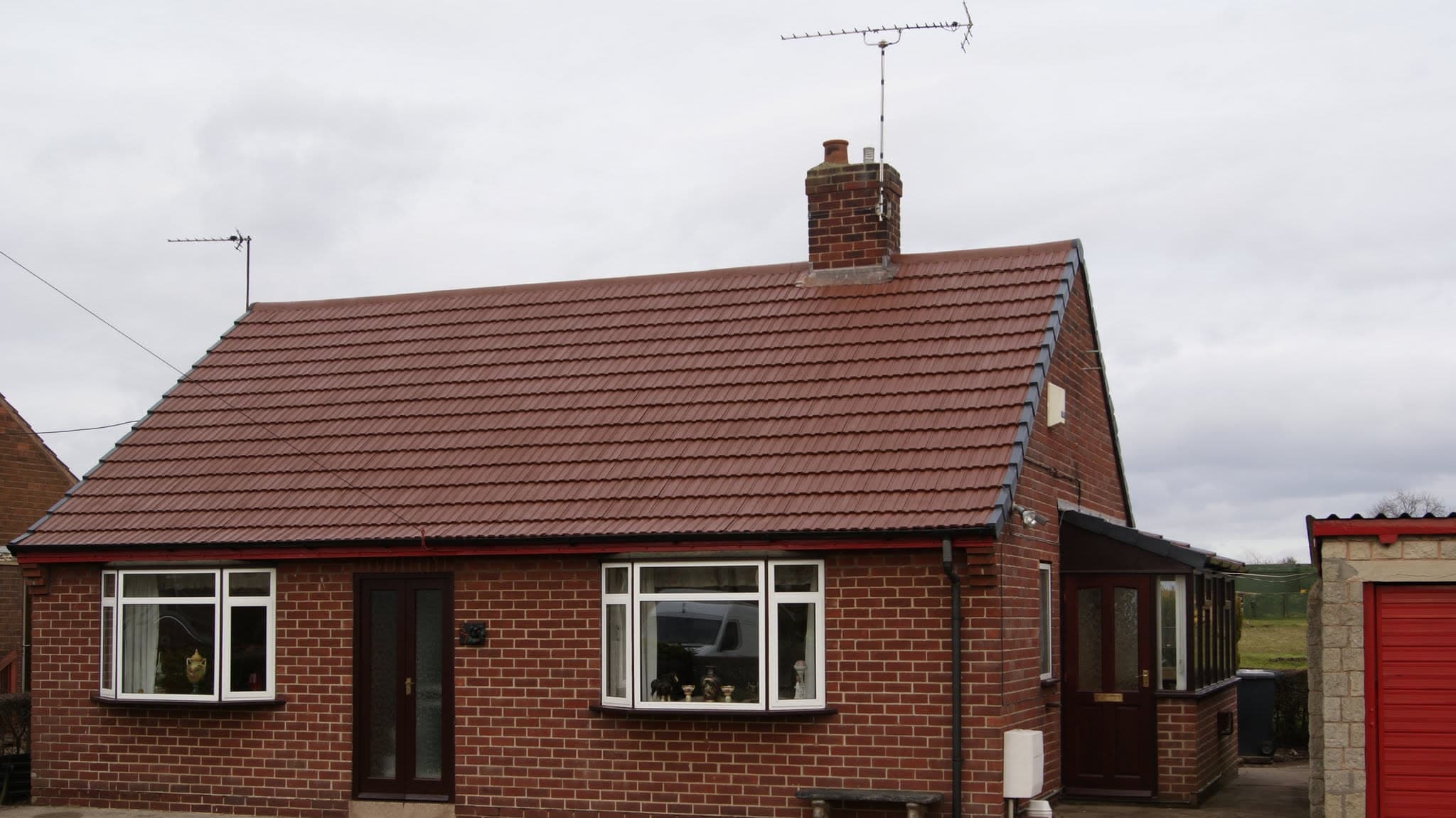 Pitched roof with terracotta concrete tiles and brick chimney stack with TV aerial