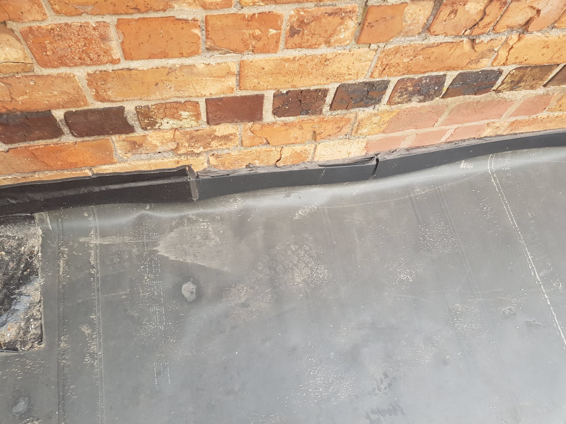 Grey flat roof with lead flashing against brick chimney stack