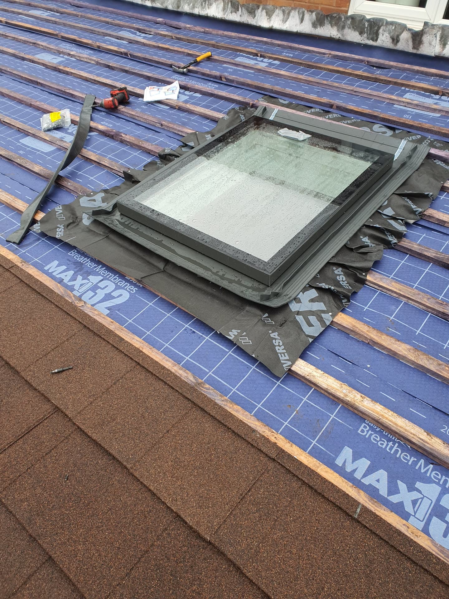 Velux roof window installation in progress on pitched roof with blue breathable membrane and battens