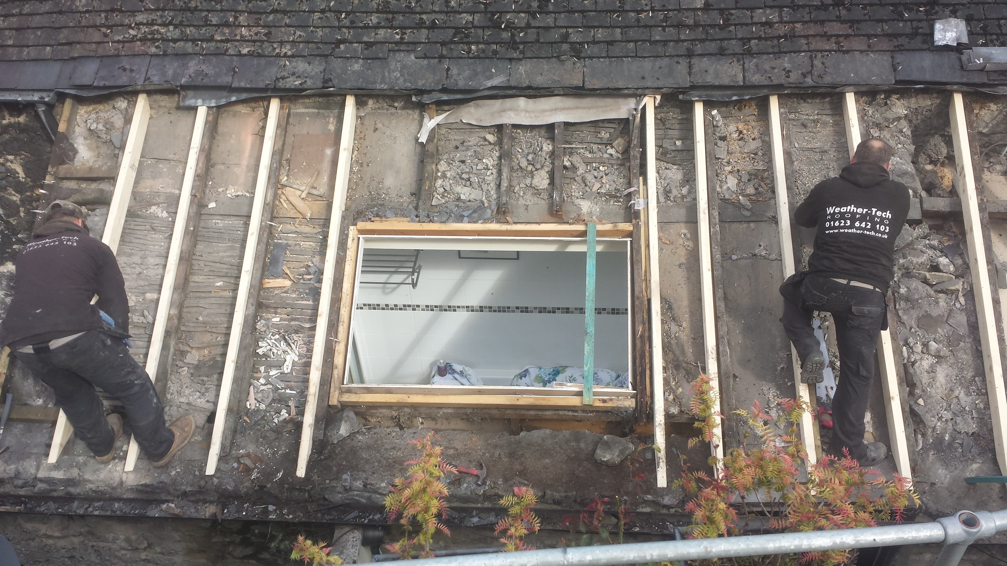 Two WeatherTech fitters working on exposed flat roof structure with skylight visible below