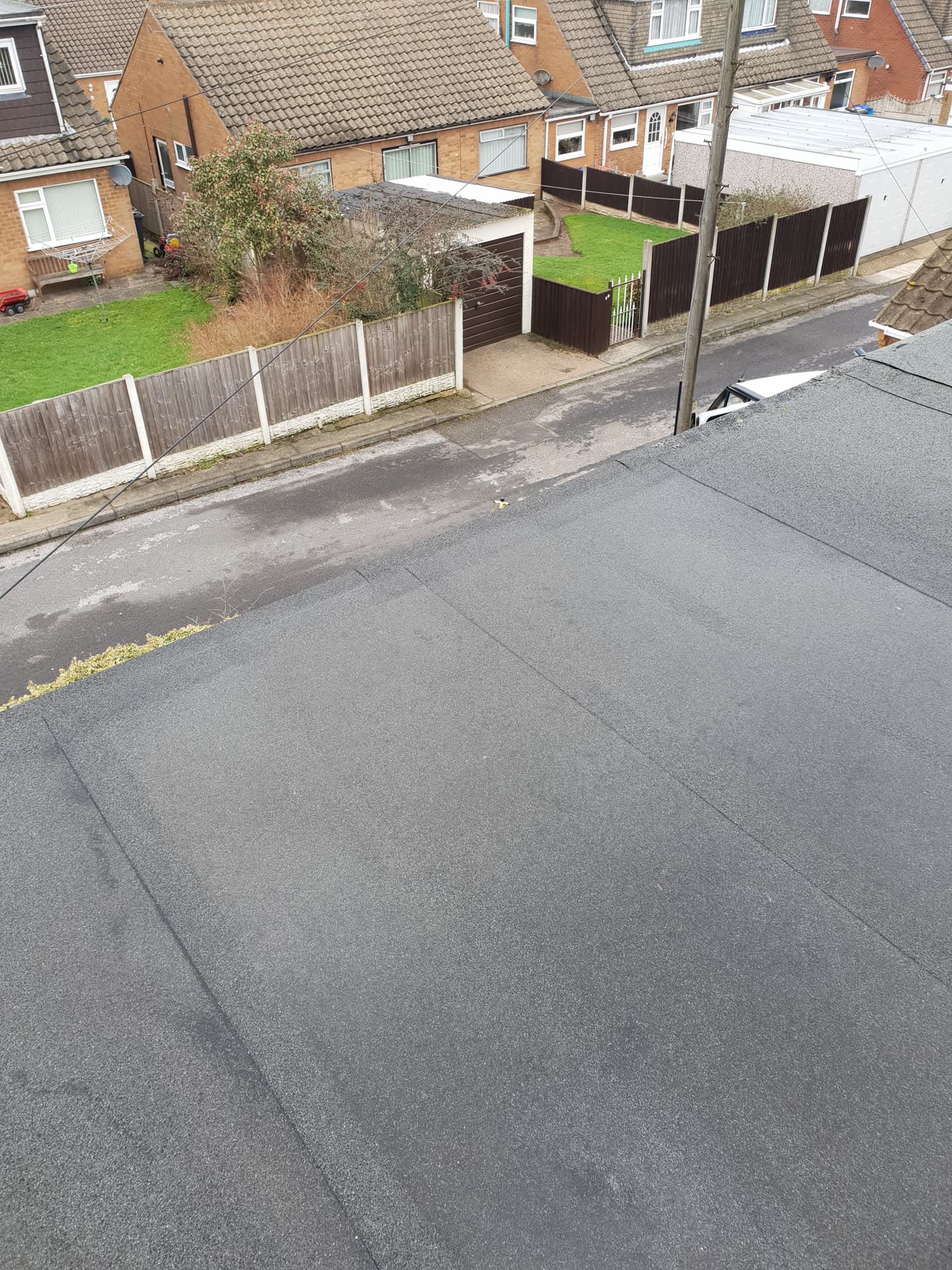 Grey felt flat roof on residential property overlooking street and neighbouring tiled roofs