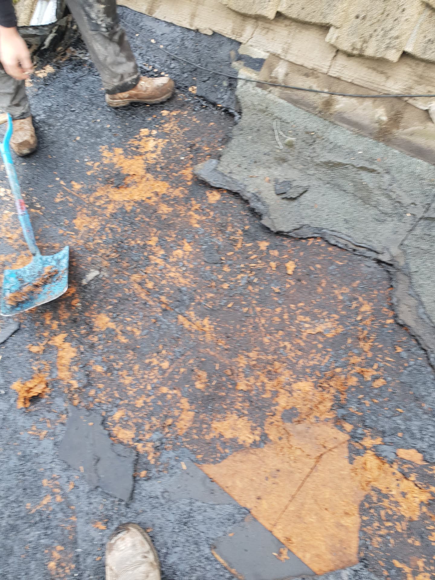 Fitter removing old felt from flat roof showing deteriorated surface