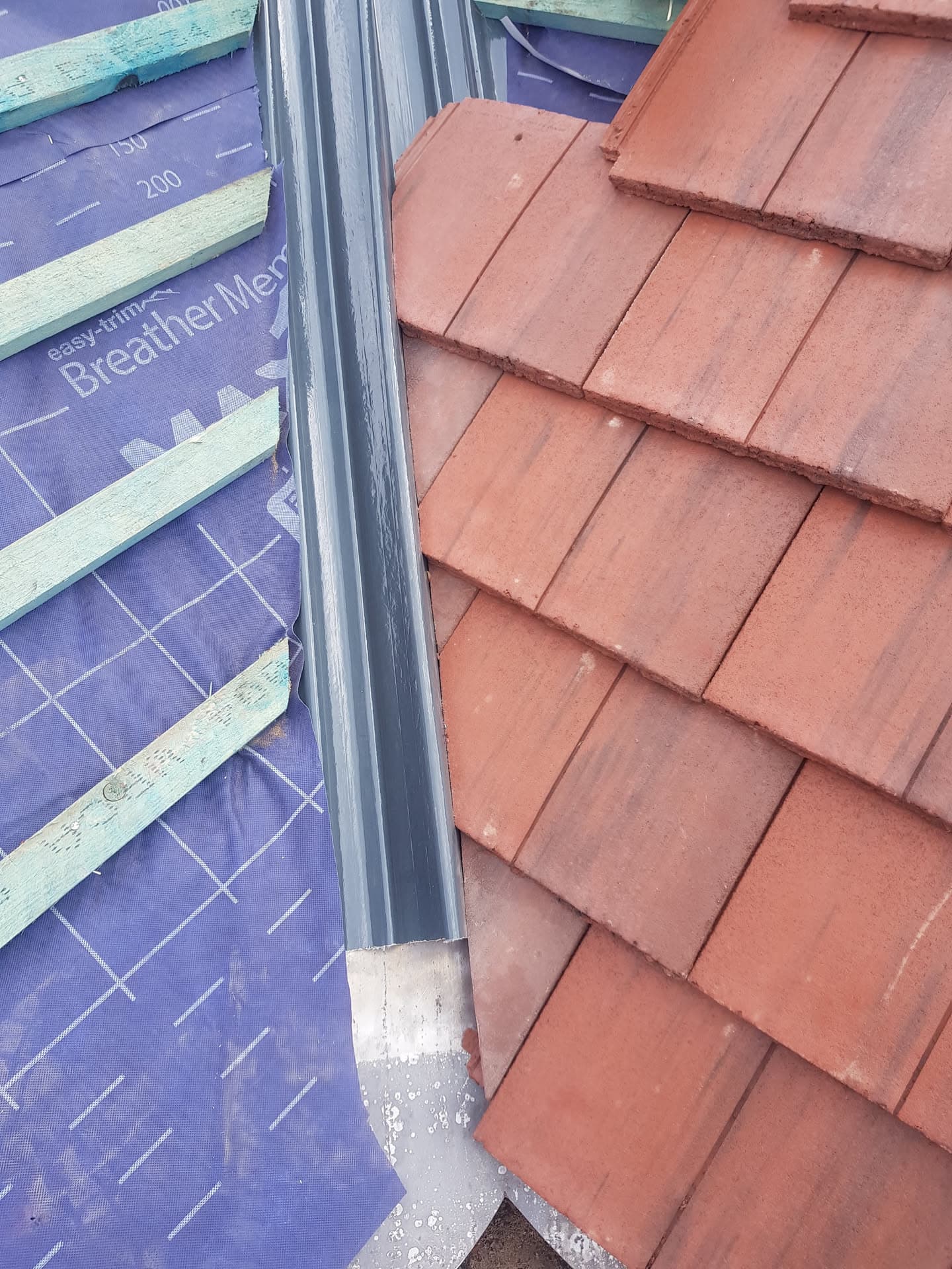 Pitched roof with terracotta clay tiles meeting breathable membrane and metal valley gutter