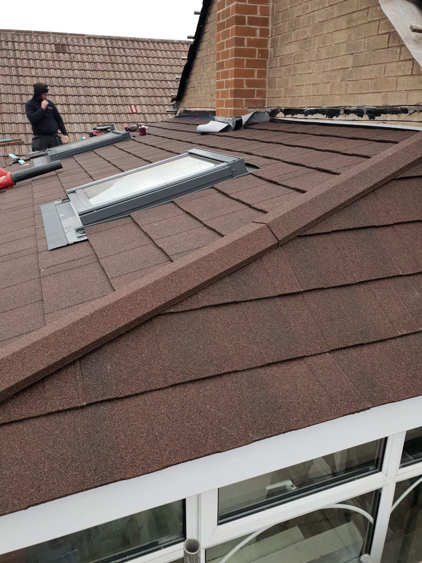 Fitter installing brown concrete tiled pitched roof with velux windows