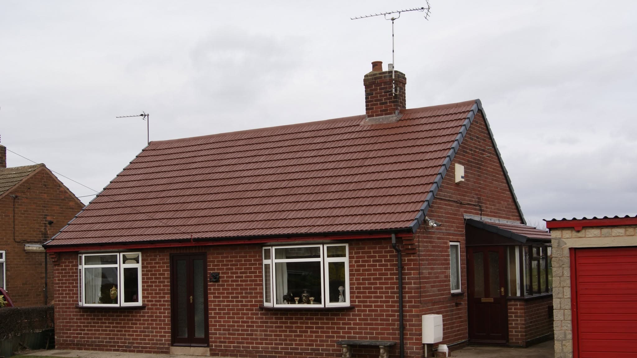 Red concrete tiled pitched roof on brick bungalow with chimney stack and TV aerial