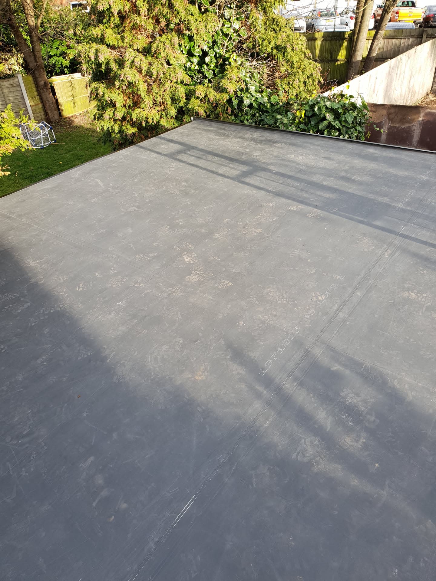 Completed grey flat roof with EPDM rubber membrane overlooking residential garden