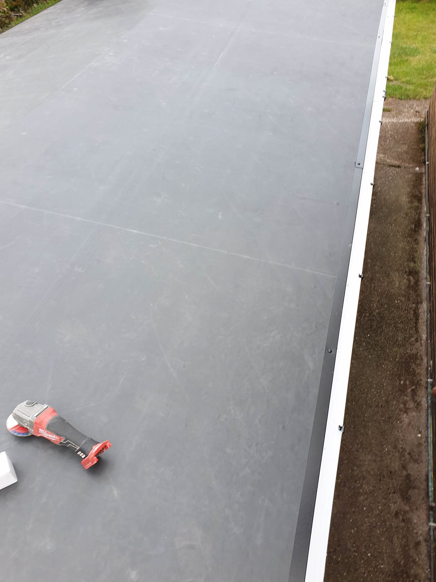 Grey EPDM rubber flat roof with white fascia trim and cordless drill