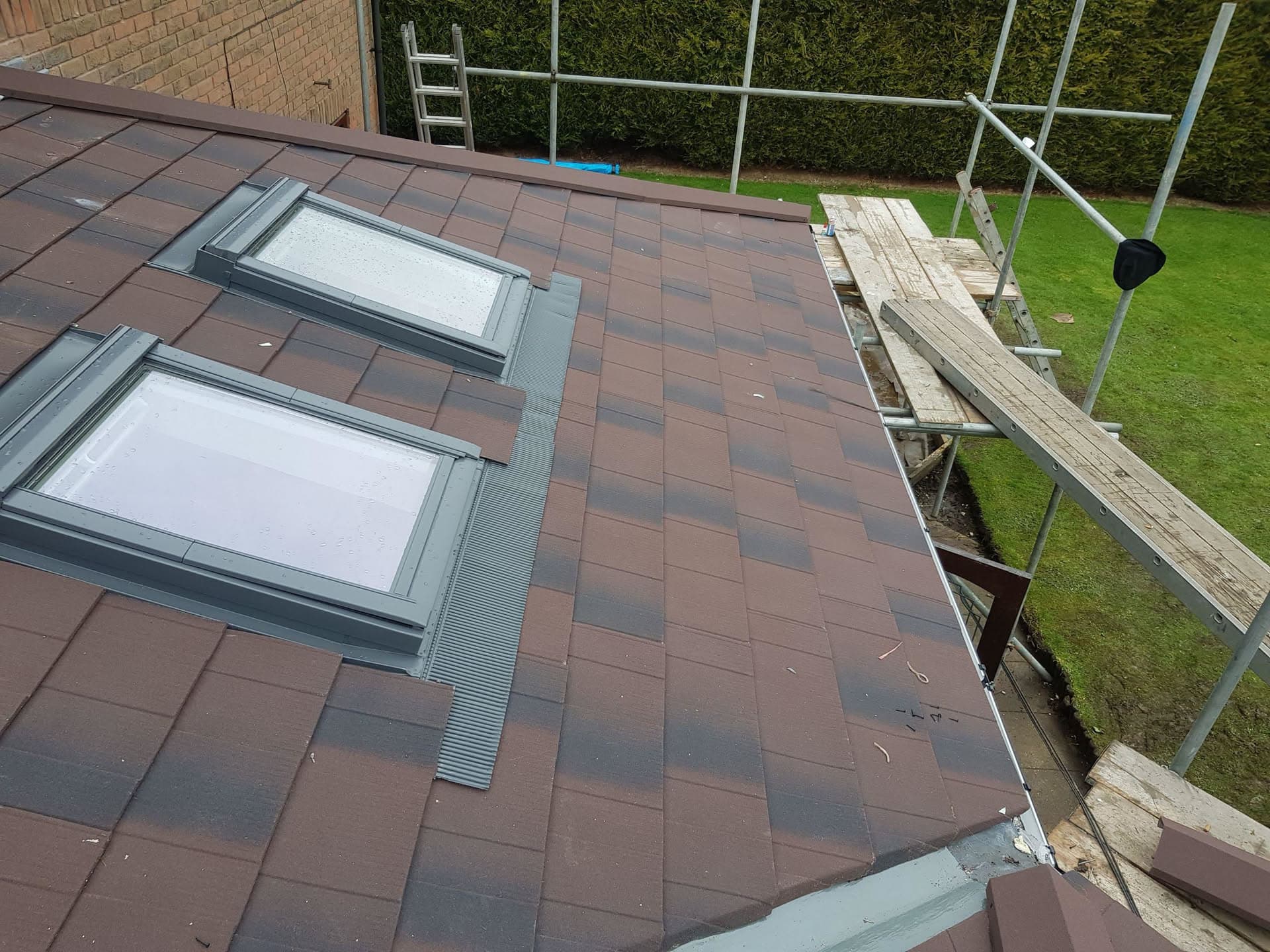 Pitched roof with brown concrete tiles and two grey-framed roof windows with scaffolding alongside
