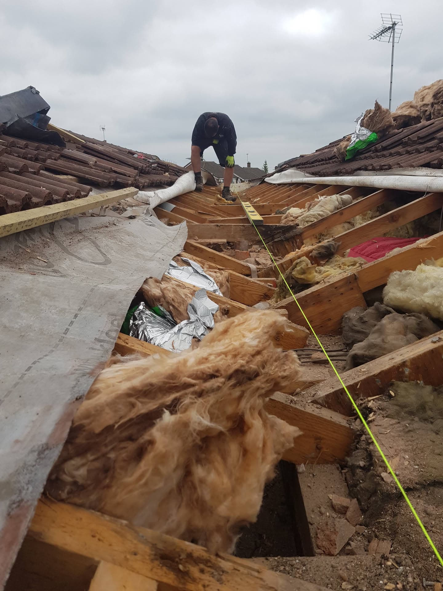 Roofer working on exposed timber rafters and joists during pitched tiled roof repair